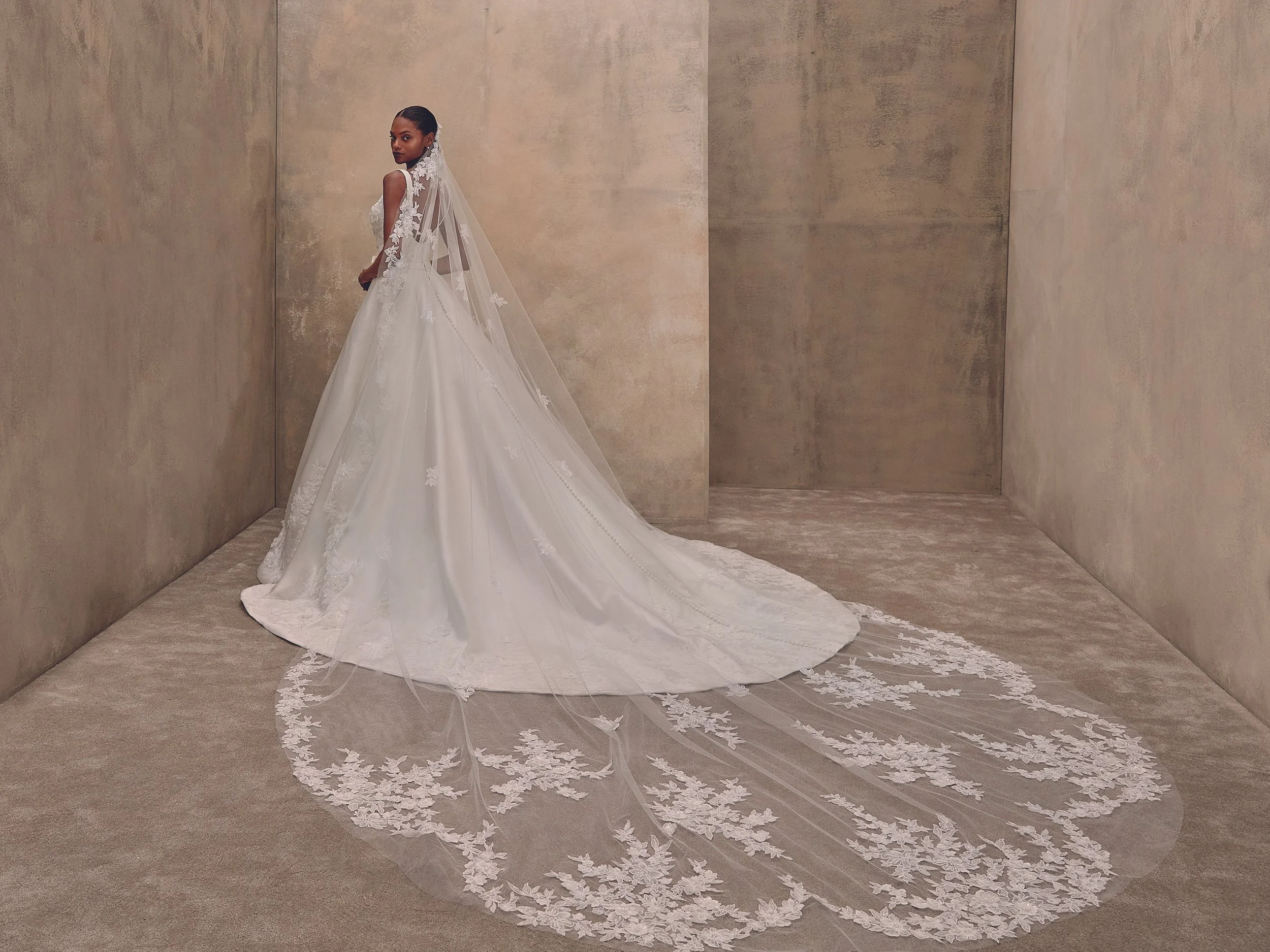 Femme portant une robe de mariée blanche avec un long train en dentelle, dans une pièce aux murs en béton