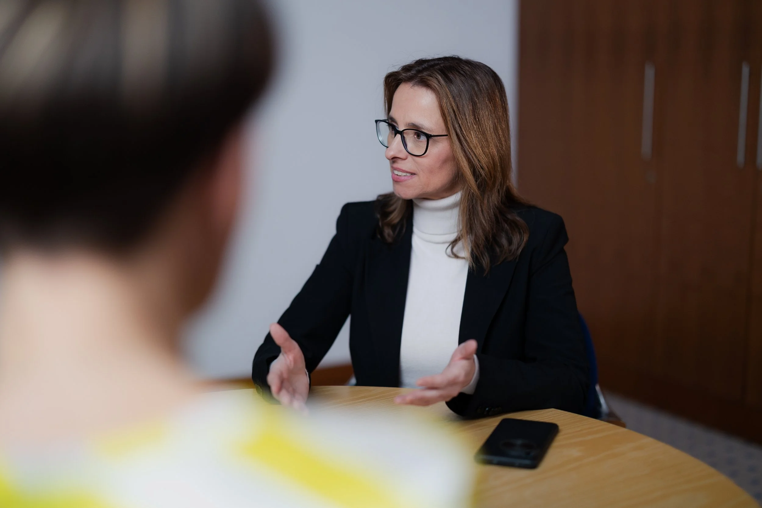 Iris Wagner spricht in einem Interview in einem Büro mit einem Mann, der nur teilweise sichtbar ist.