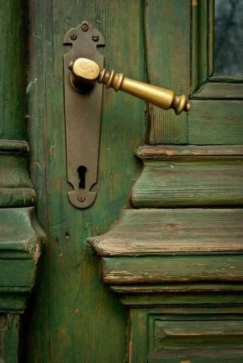 An old green wooden door with a gold-colored door handle and an ornate keyhole.