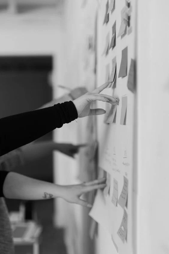 Person arranging sticky notes on a whiteboard in a meeting or planning session.