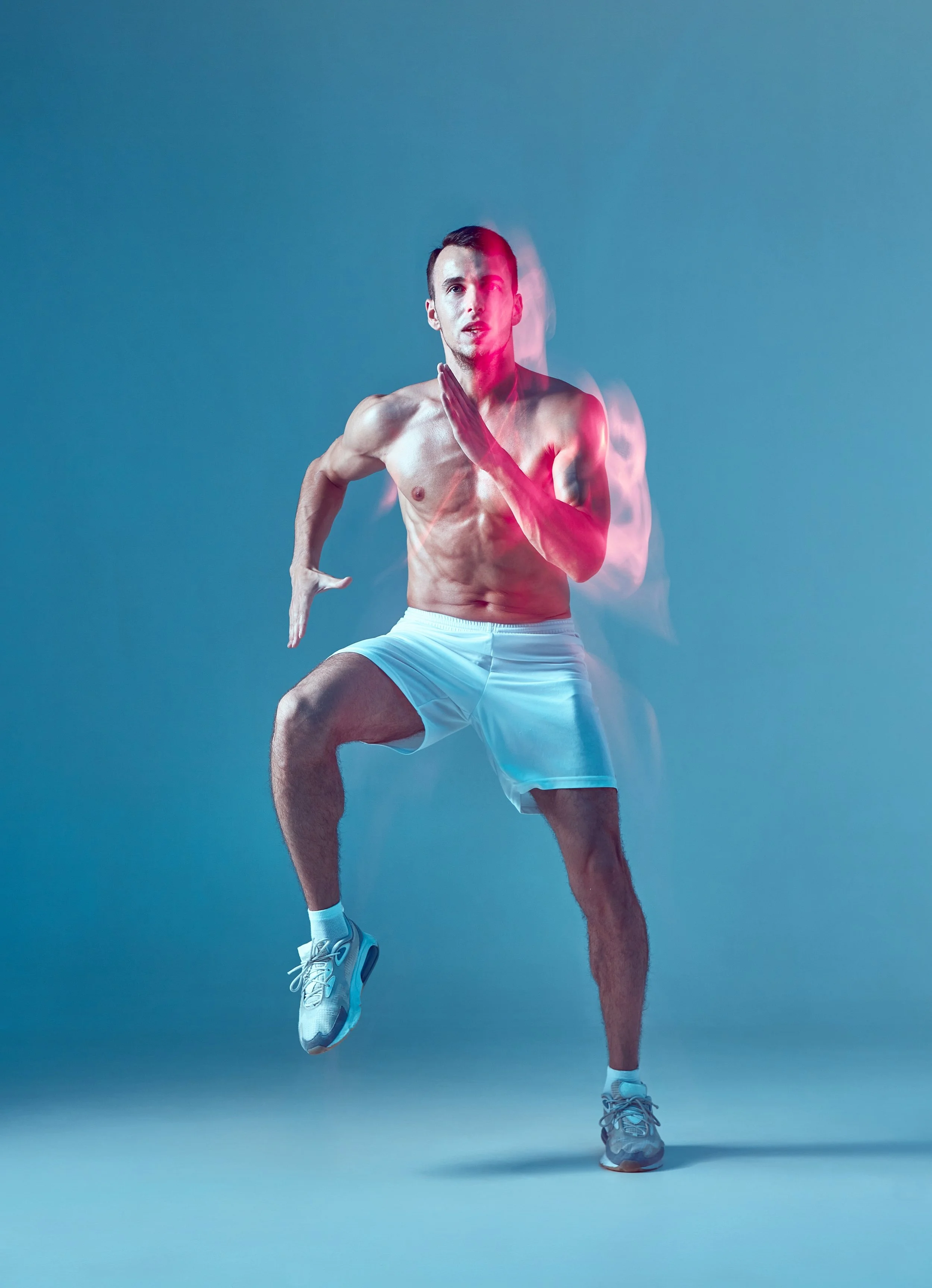 Ein junger Mann in weißen Shorts und Laufschuhen, der in einer Laufbewegung auf einem grauen Hintergrund läuft, mit einer leichten Bewegungsunschärfe in der Mitte des Bildes.