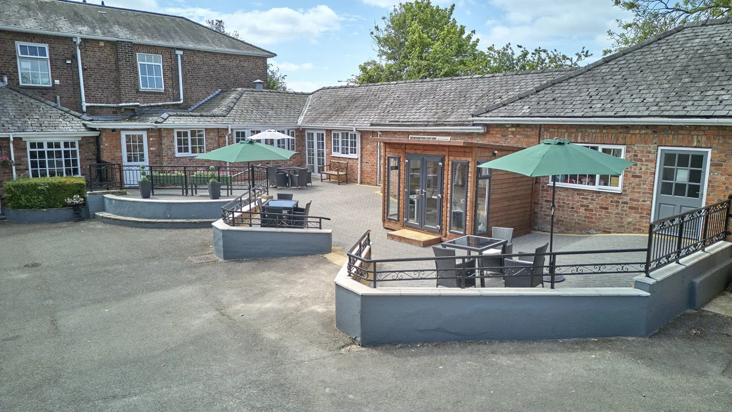 Outdoor patio area with tables, chairs, and umbrellas, surrounded by brick buildings and a concrete walkway.