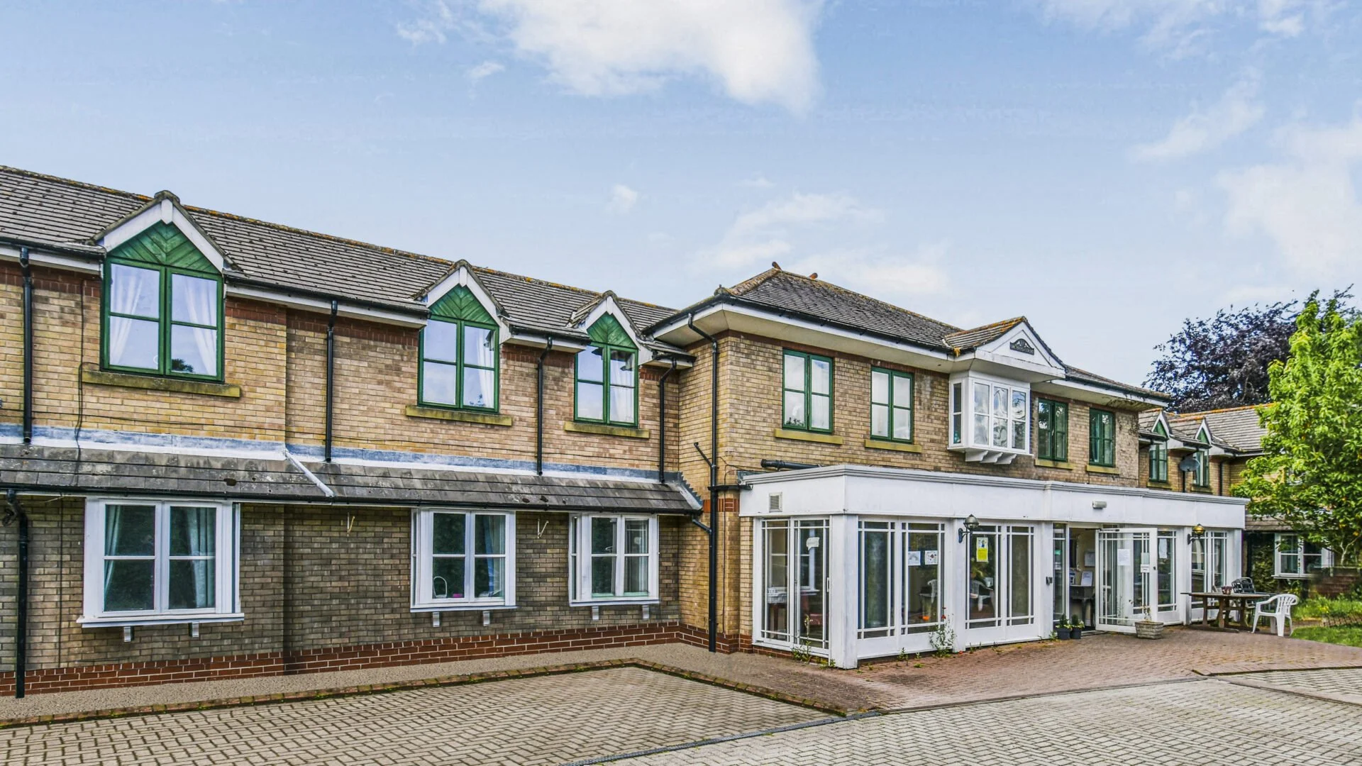 A two-story brick apartment building with green window frames and a glass-enclosed porch at the entrance.