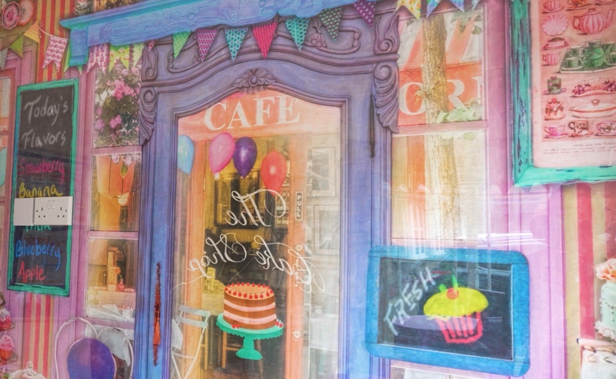 Colorful cafe storefront with pink striped walls, purple ornate door frame, chalkboard menu featuring flavors like strawberry, banana, blueberry, and apple, decorated with balloons, bunting, and artwork of a cake and a cupcake.
