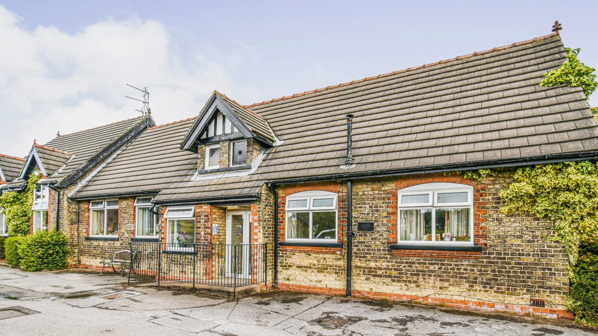 A row of old brick houses with tiled sloped roofs, multiple windows, and ivy growing on the right side.