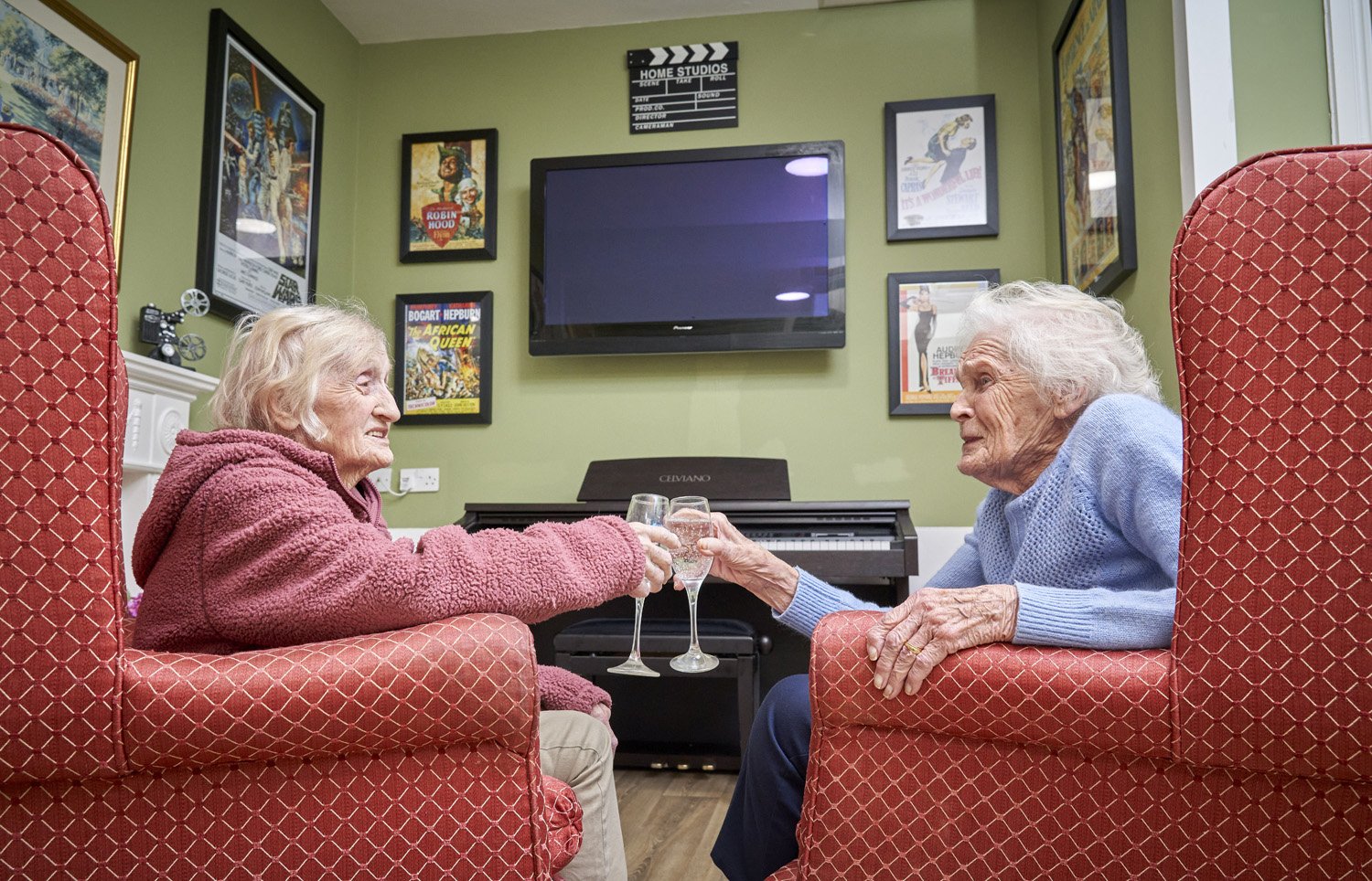 Two elderly women enjoying drinks and toasting in a cozy, decorated living room.