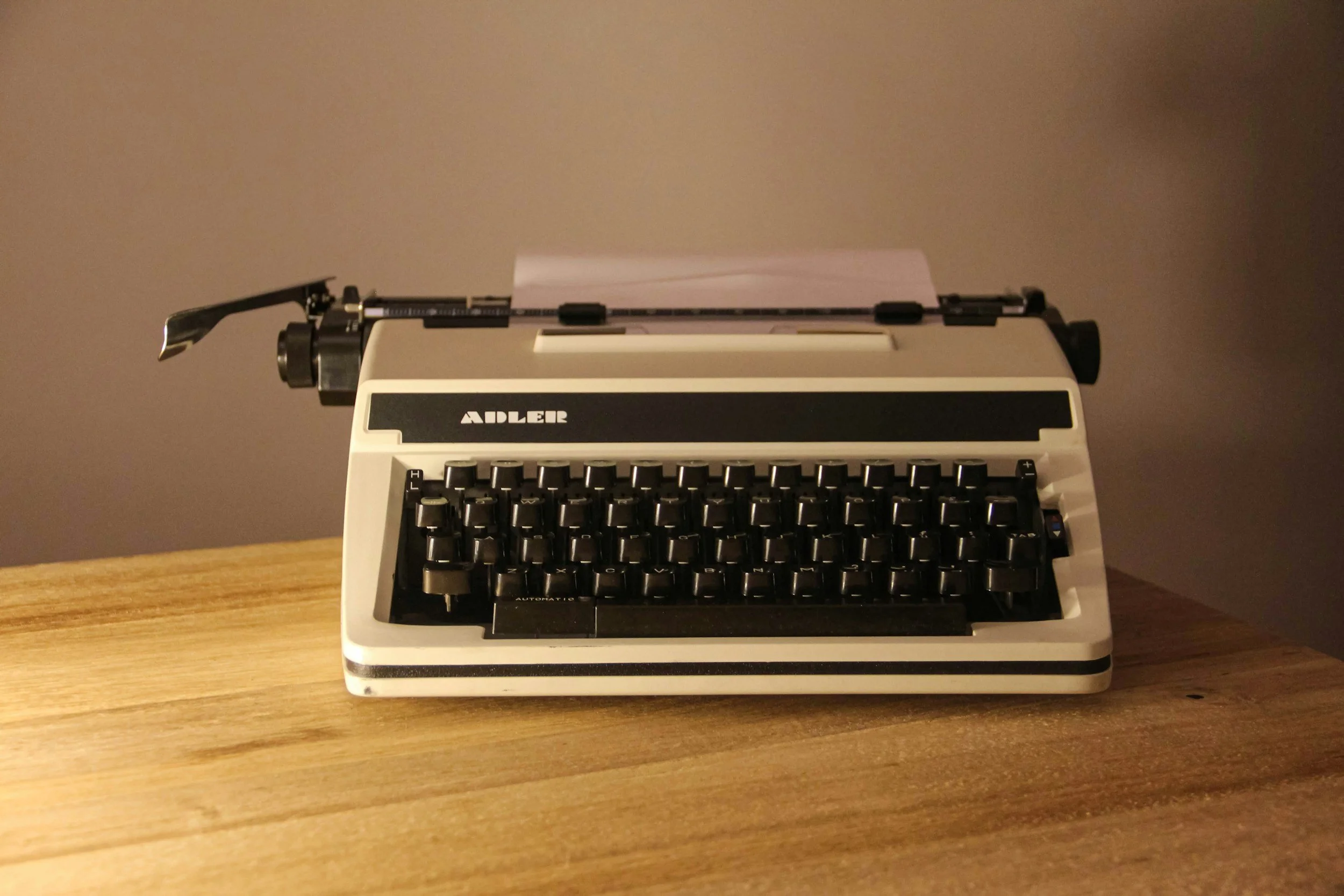 A beige vintage typewriter with black keys, labeled 'Adler', placed on a wooden surface.