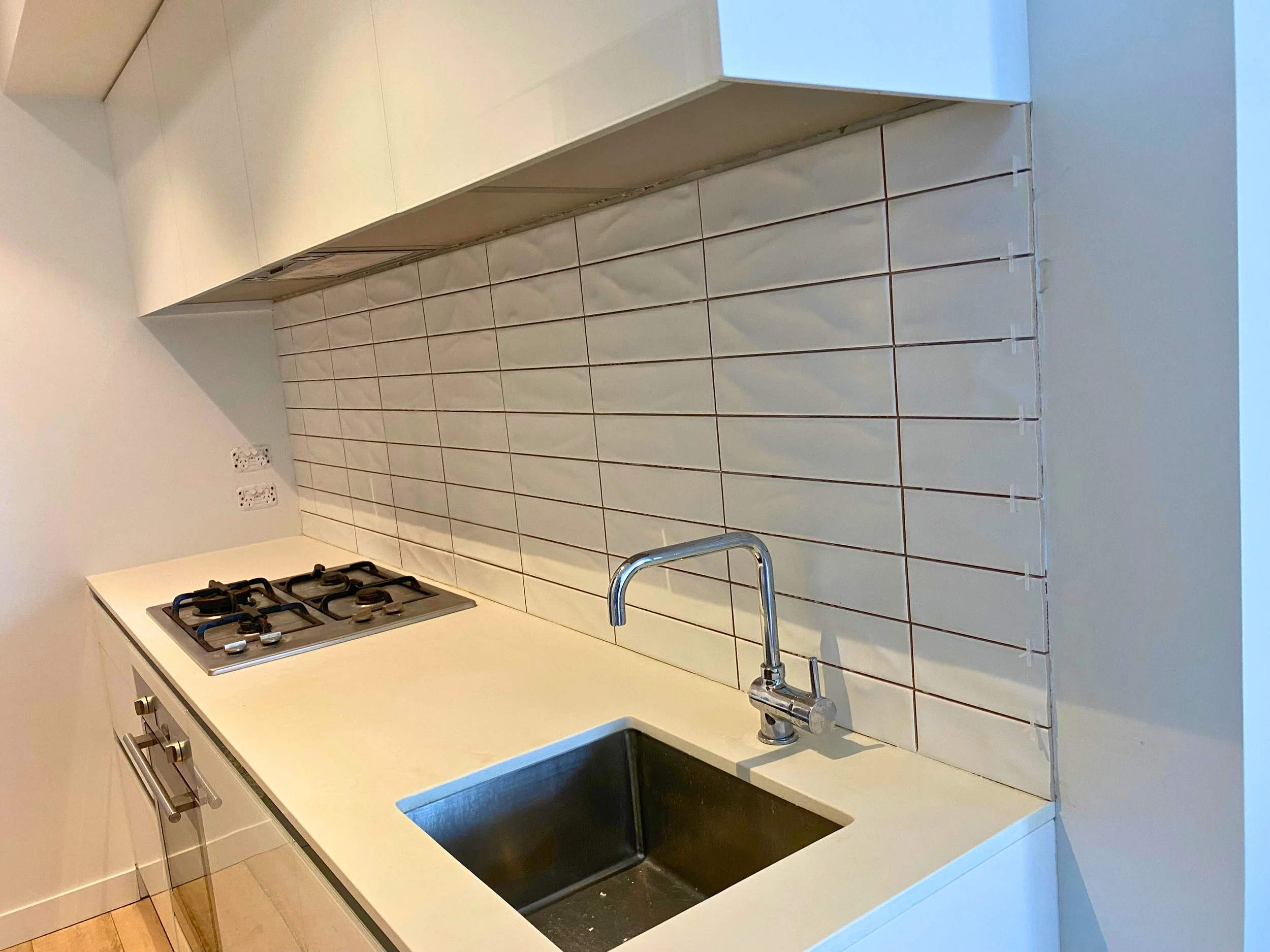 A modern kitchen countertop with a built-in gas stove, a stainless steel sink, and a white tiled backsplash.