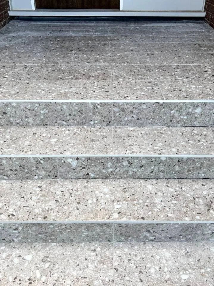 Five stone steps leading up to a glass door with metal framing.