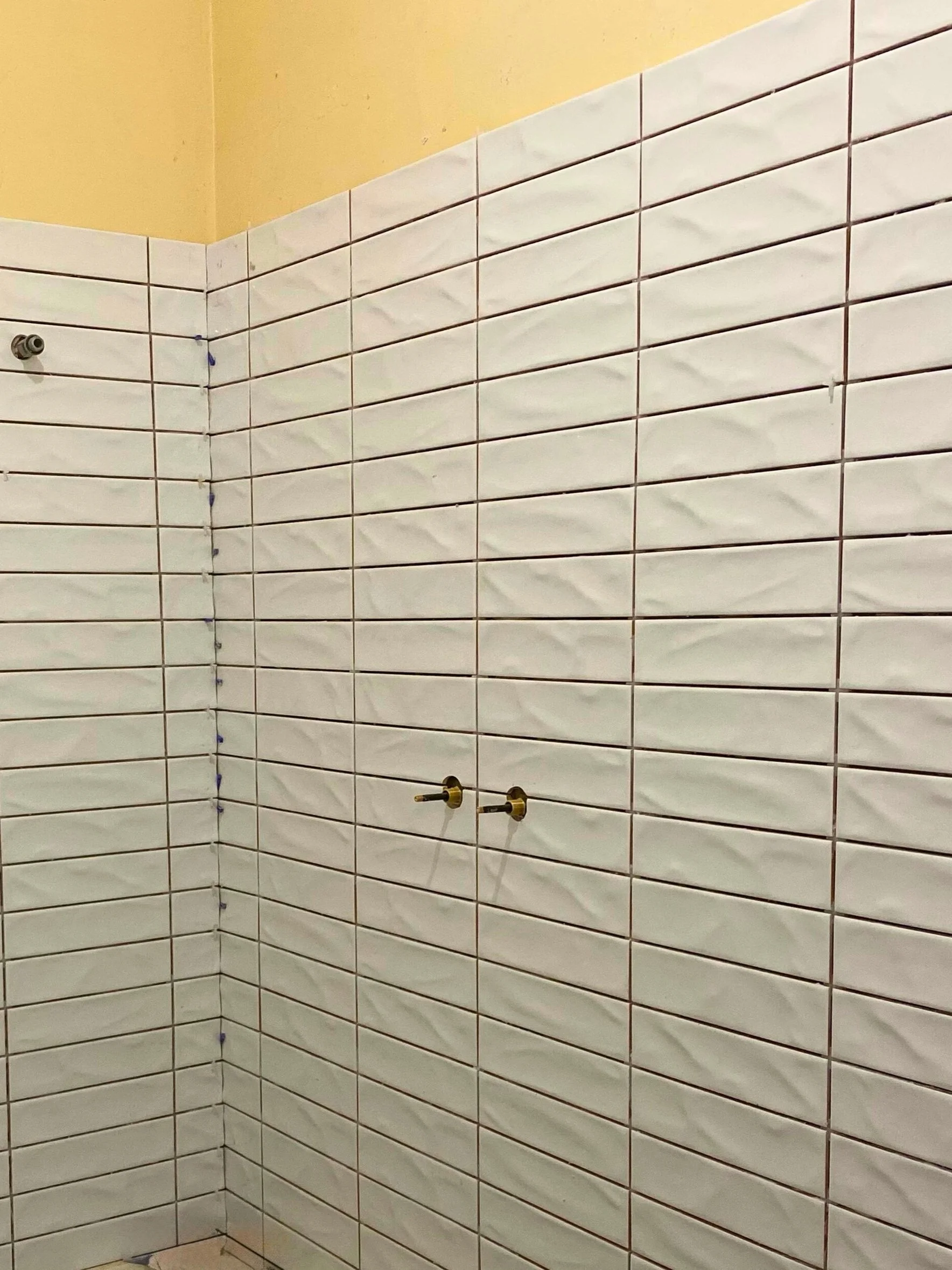 White tiled bathroom wall with brass fixtures and a beige ceiling.