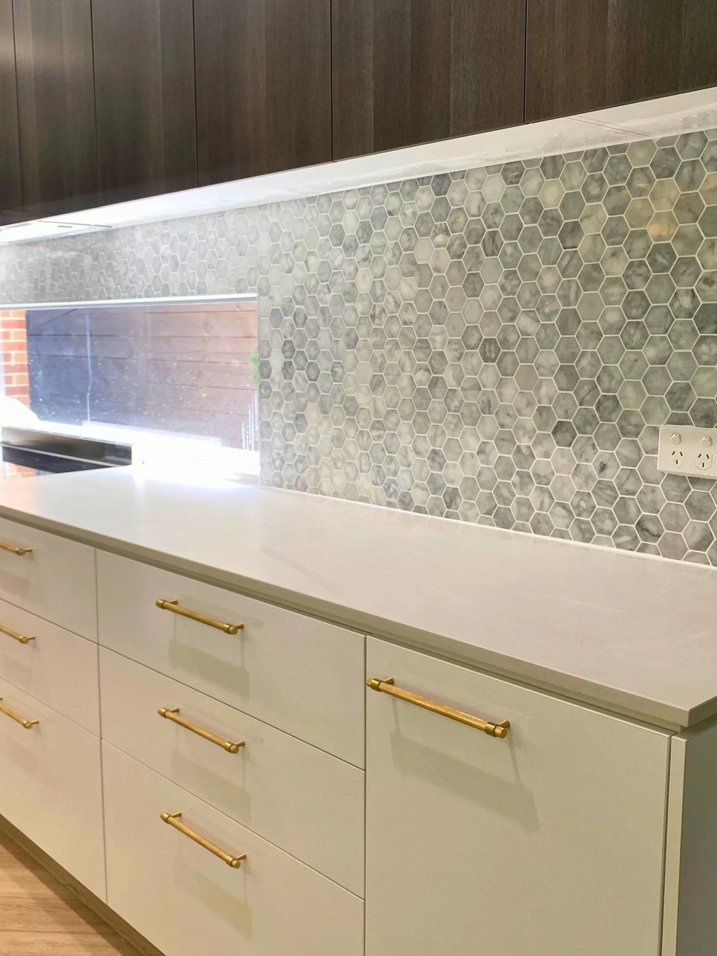 Kitchen countertop with white cabinets, gold handles, hexagon tile backsplash, and electrical outlet.