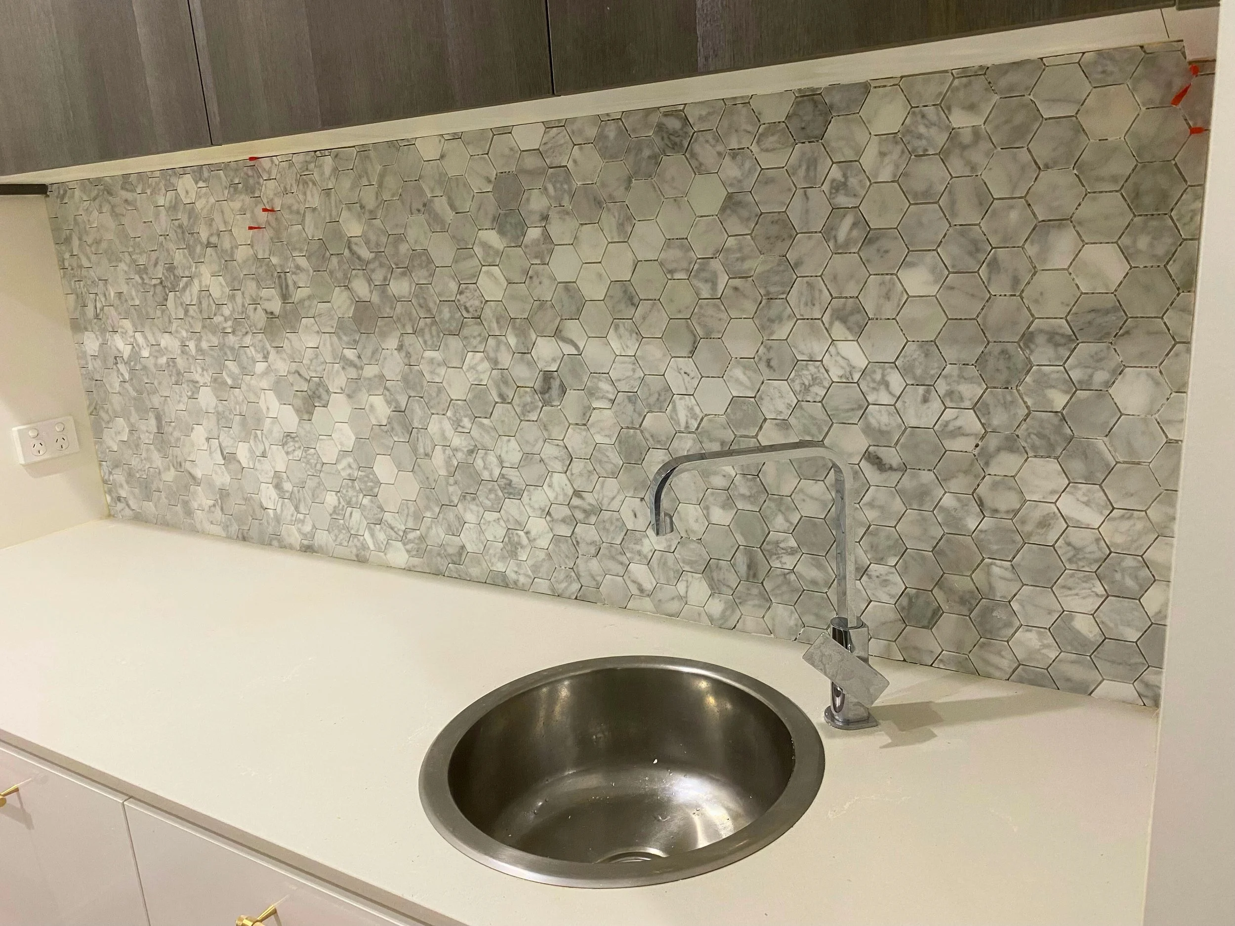 Kitchen countertop with a stainless steel sink and modern hexagonal marble tile backsplash.