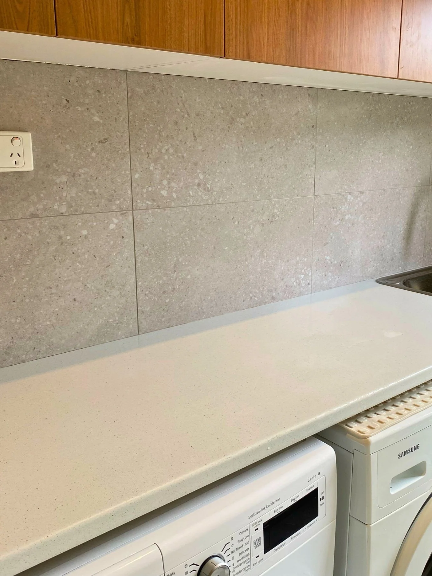 A beige countertop with a speckled beige backsplash, a white washing machine, and a white Samsung dryer in a laundry room.