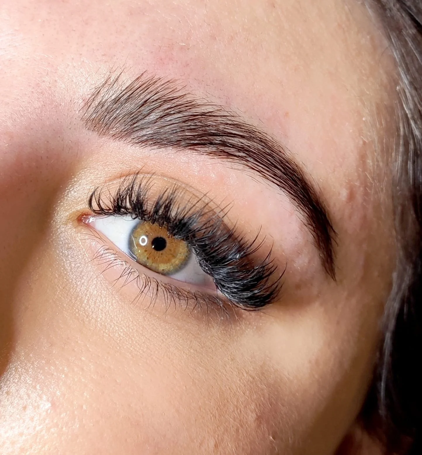 Nahaufnahme eines menschlichen Auges mit braunem Iris und langen Wimpern.