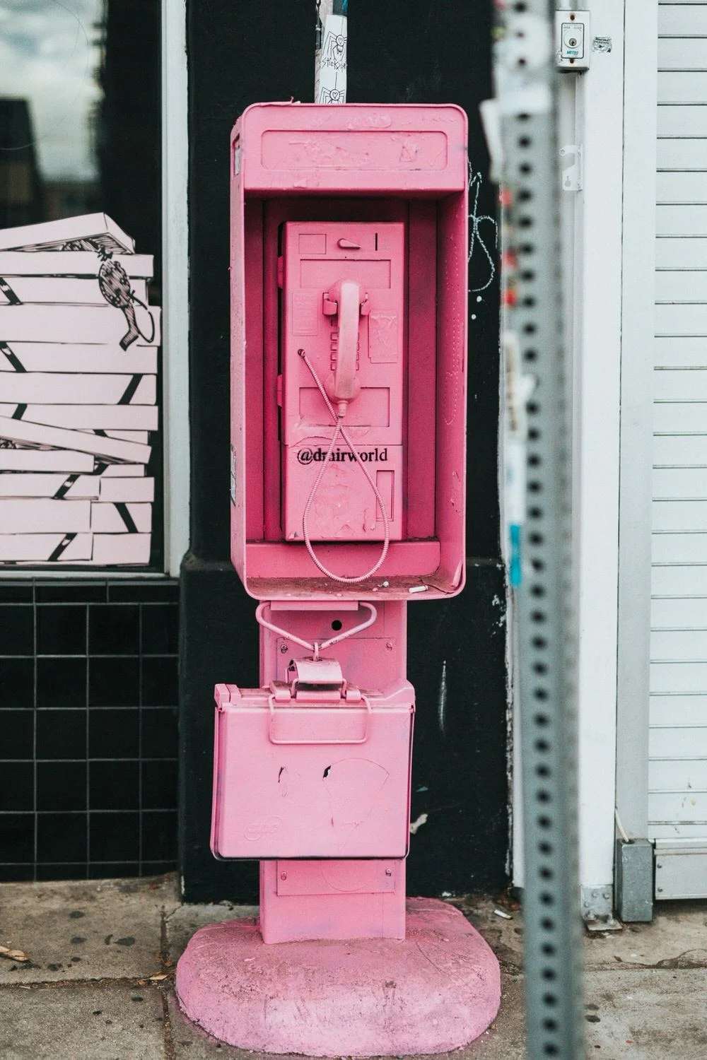 Pink vintage public telephone booth with a receiver and a coin box on the sidewalk.