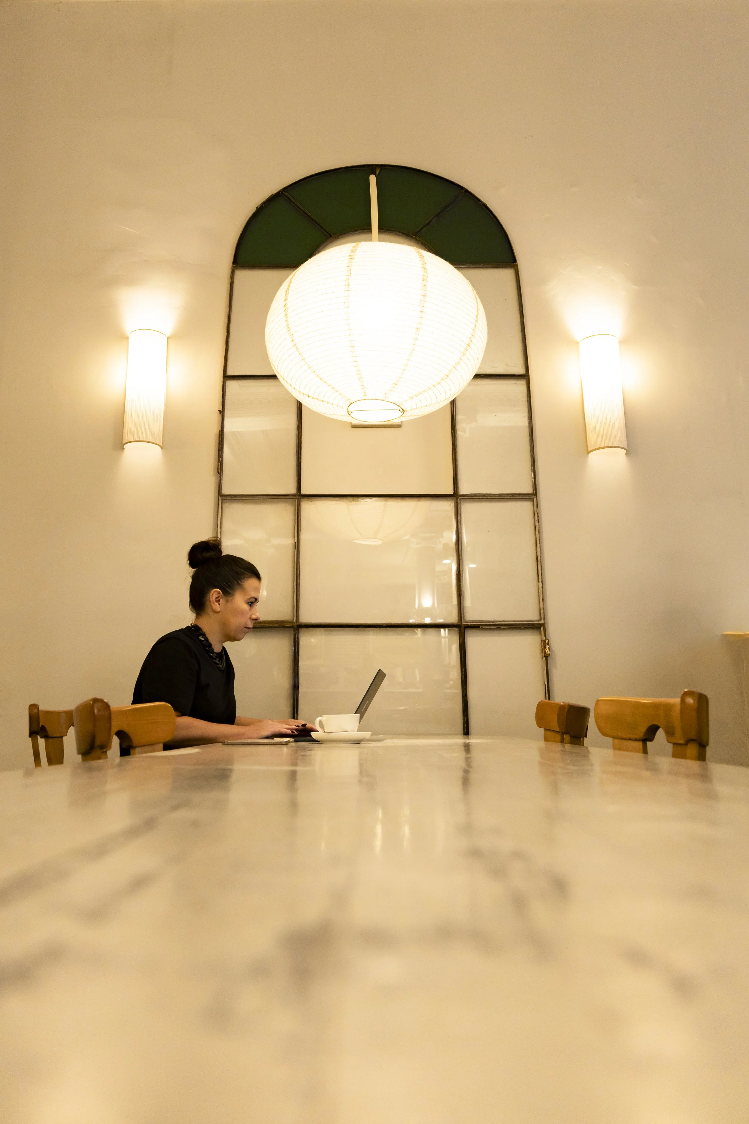 Alex Elliott sitting at a marble table in a well-lit room, working on a laptop with a cup of coffee nearby.