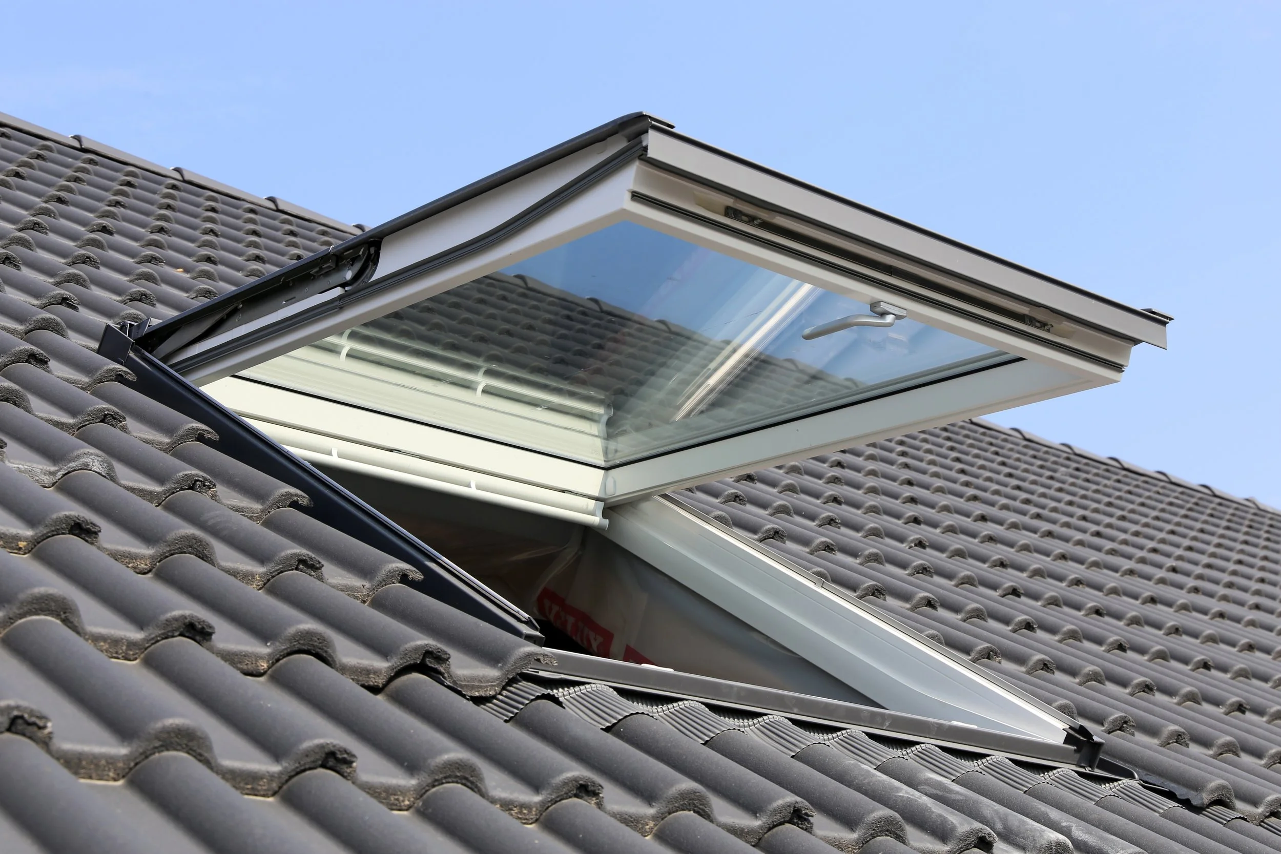 Open roof window on a tiled house roof showing the sky outside.