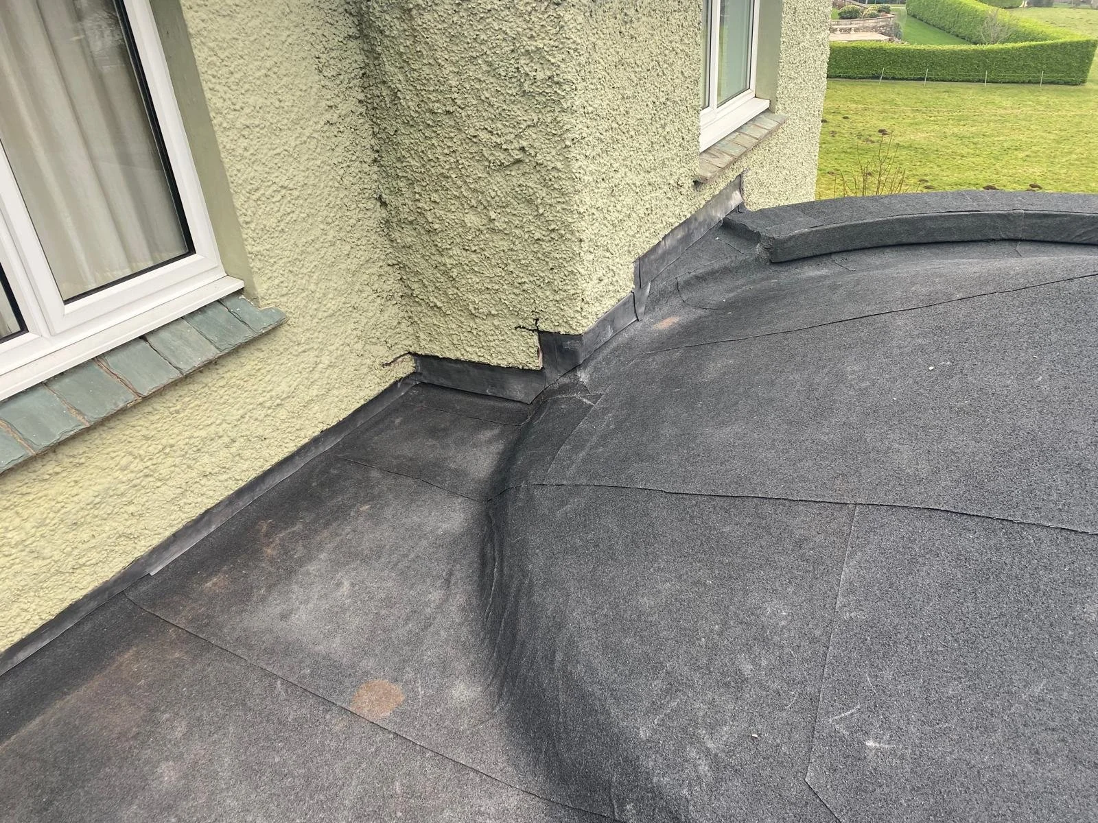 Roof edge and gutter area with damaged flashing and black waterproof membrane around a window on a yellow textured exterior wall.