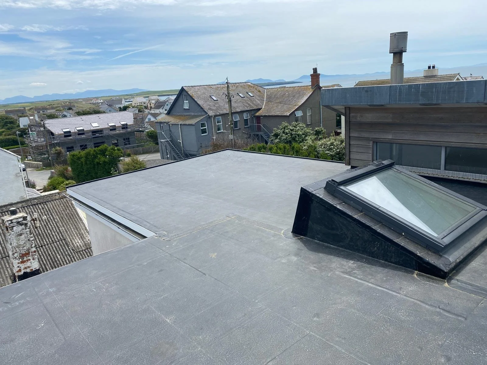 View of rooftops and houses in a coastal area with mountains in the distance, including skylights and chimneys.