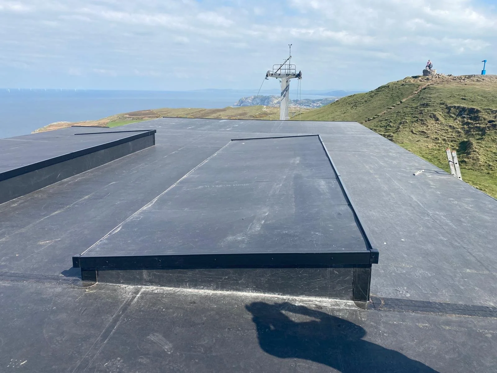 Roof with solar panels, hills, grass, and a view of the coastline in the distance.