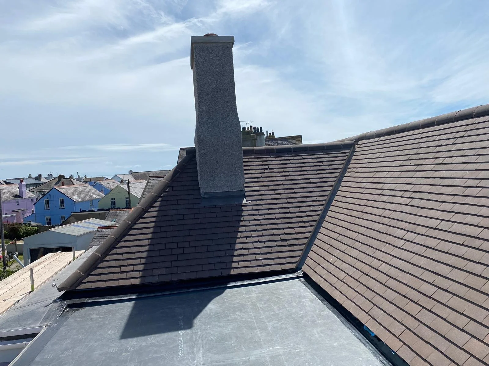 Rooftop with chimney and neighboring colorful houses under blue sky