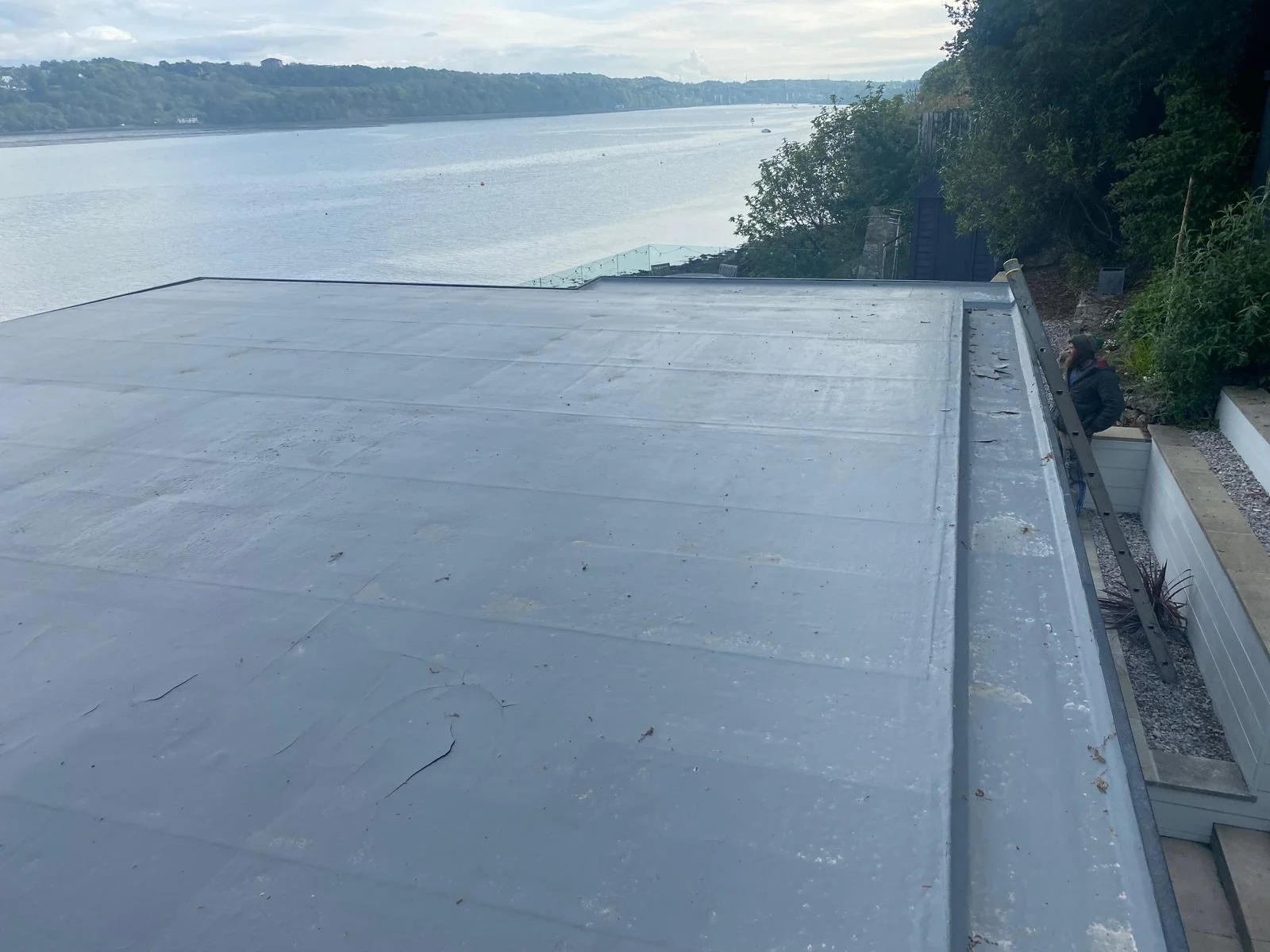 A metal roof overlooking a large river with trees on the opposite bank, and a person standing near the edge of the roof.