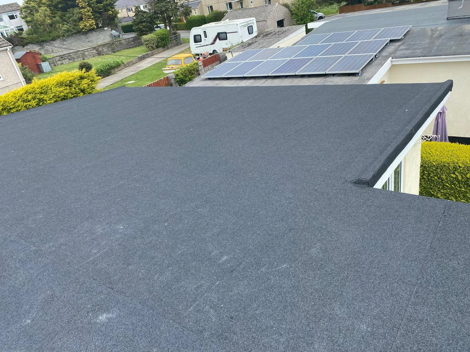 View of a house roof with newly installed black roofing material and solar panels on an adjacent roof.