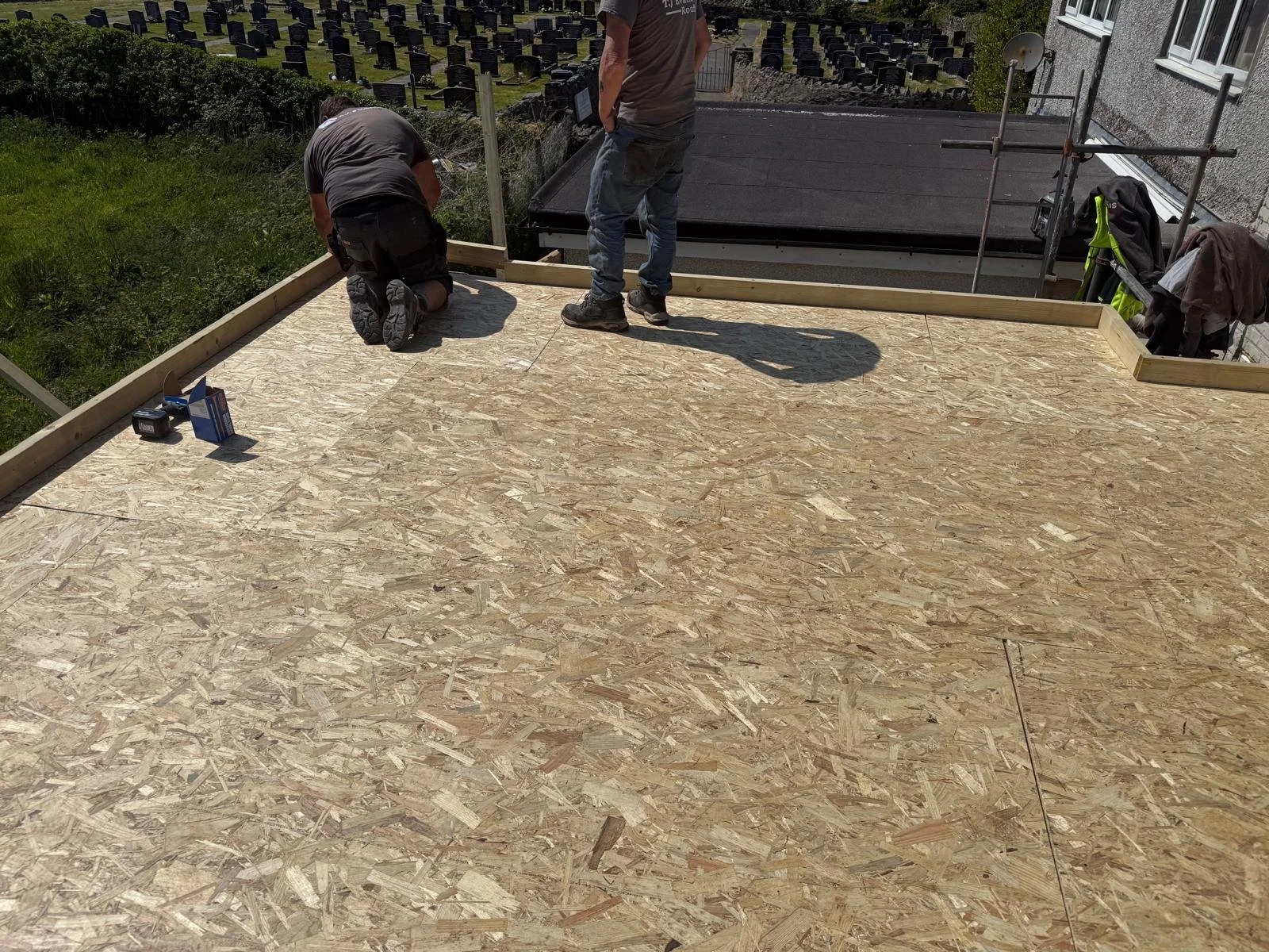 Two construction workers installing wooden framing on a plywood floor on an outdoor deck.