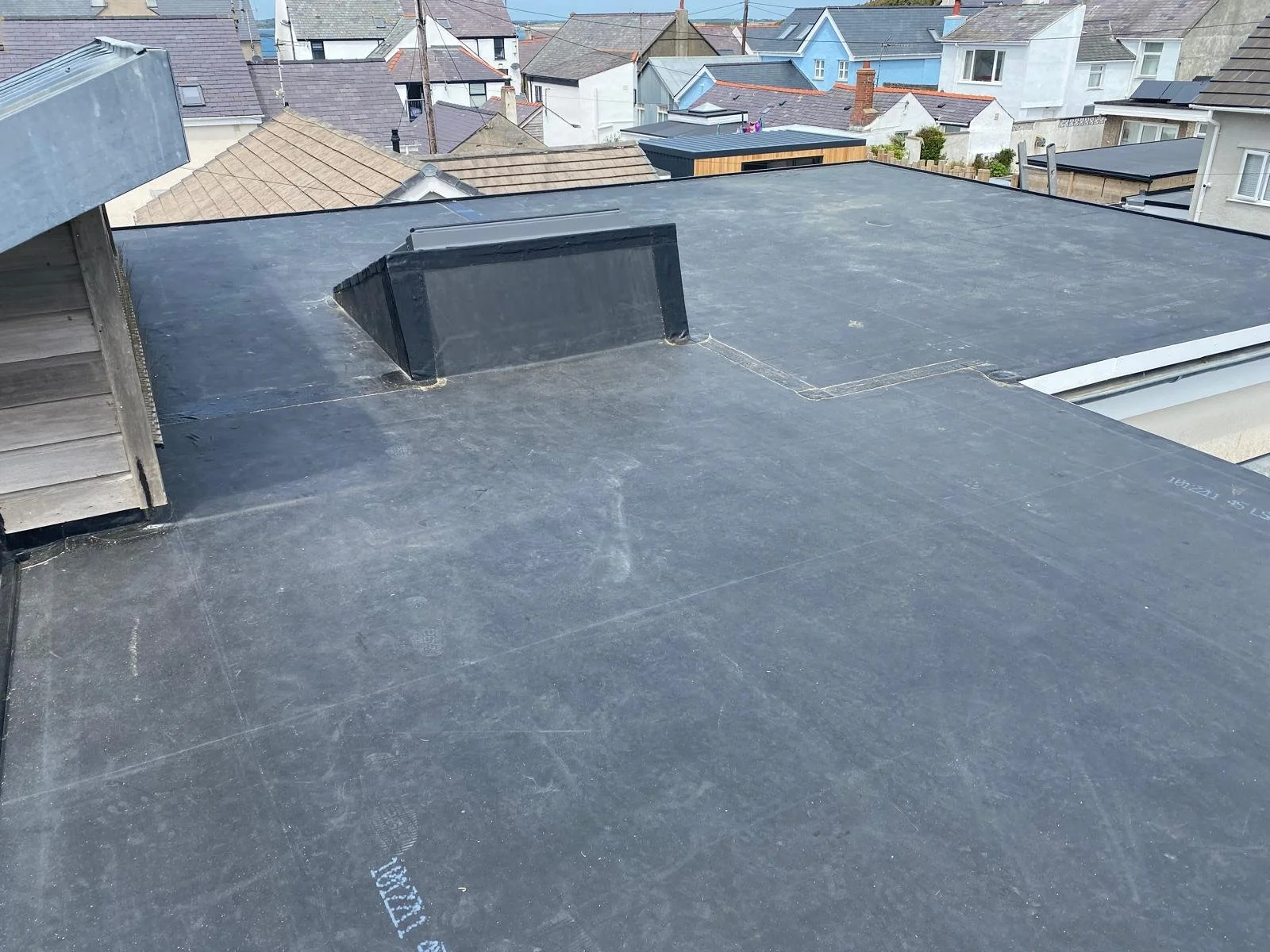 Flat black roof with a vent pipe and surrounding rooftops in a residential neighborhood.