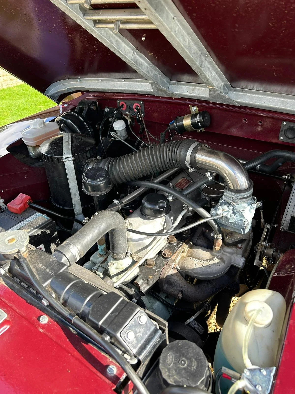 Close-up of a vintage car engine with various hoses, wires, and metal components in a red engine bay.