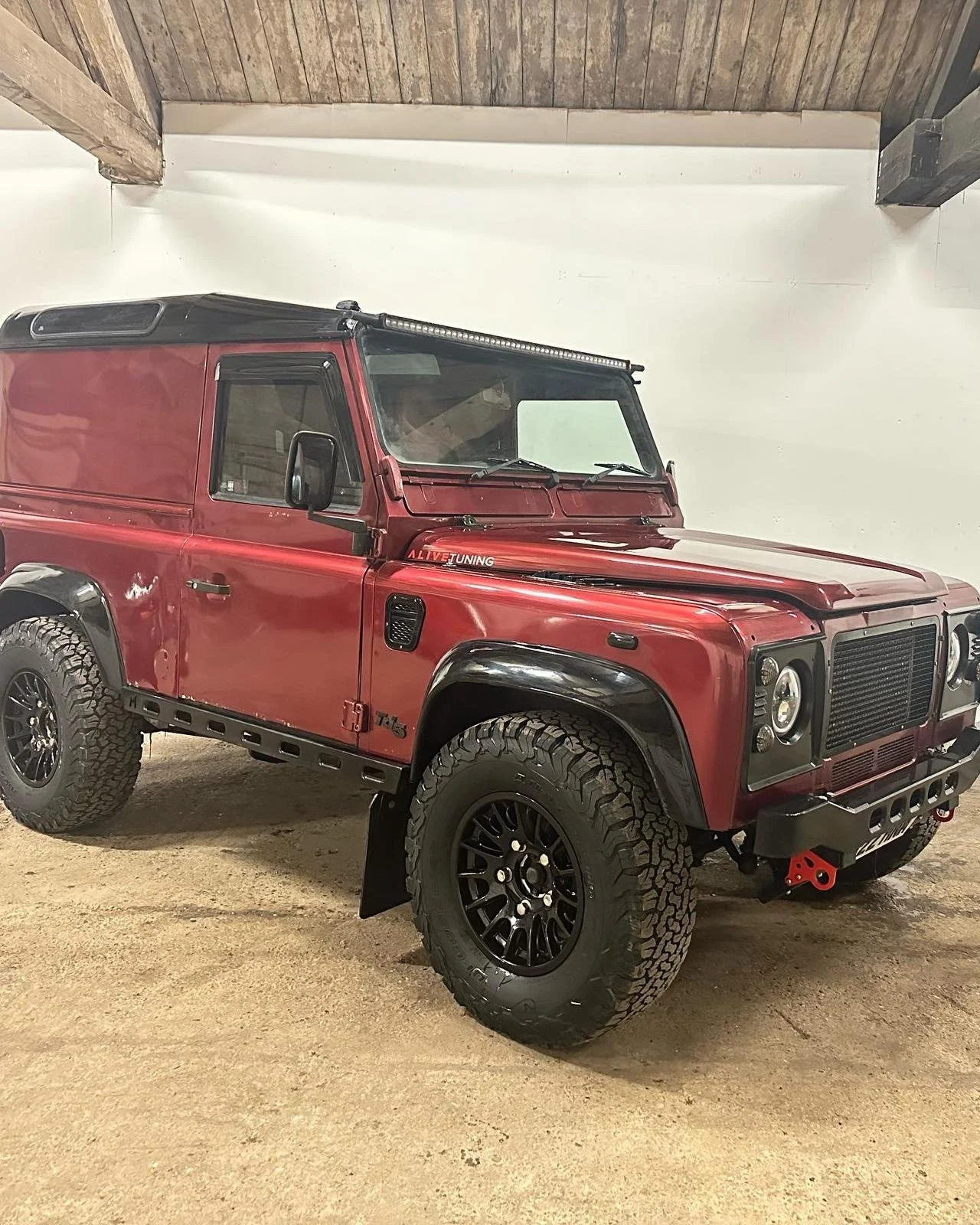 Red off-road vehicle with large tires and black accents parked indoors on a dirt floor.