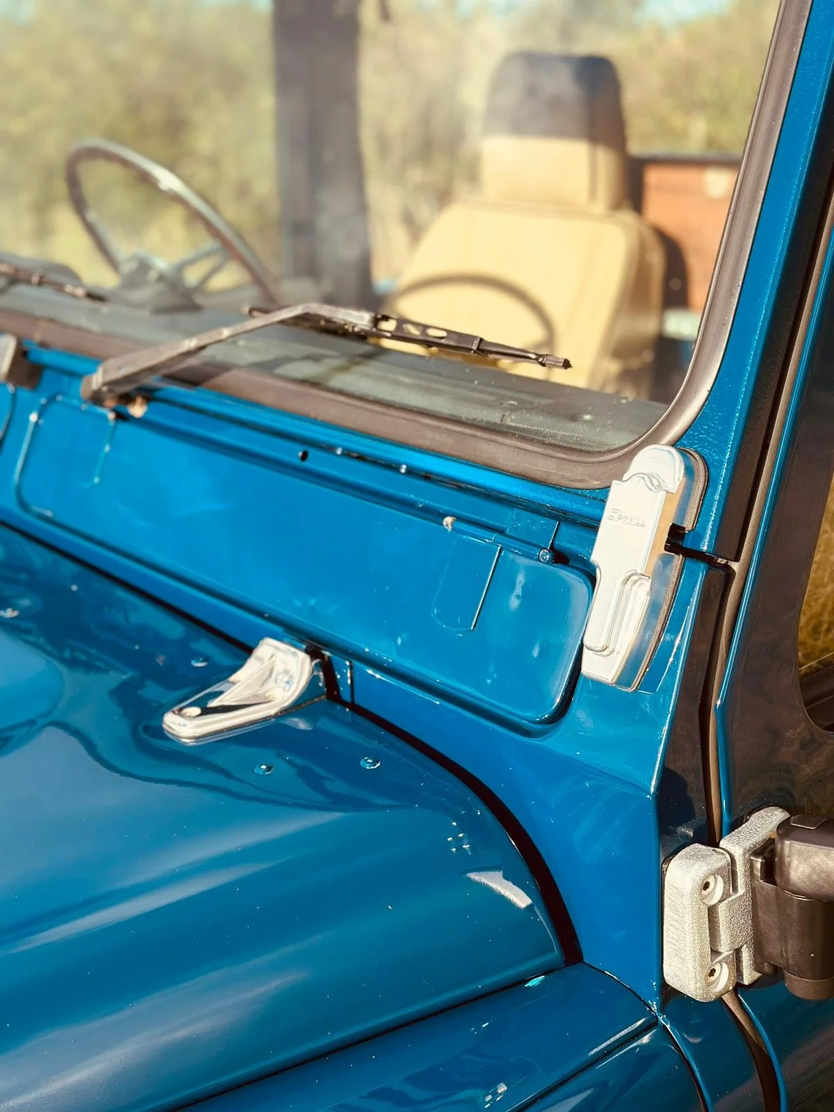 Close-up of the front part of a vintage blue vehicle, showing the windshield, side mirror, and part of the dashboard.
