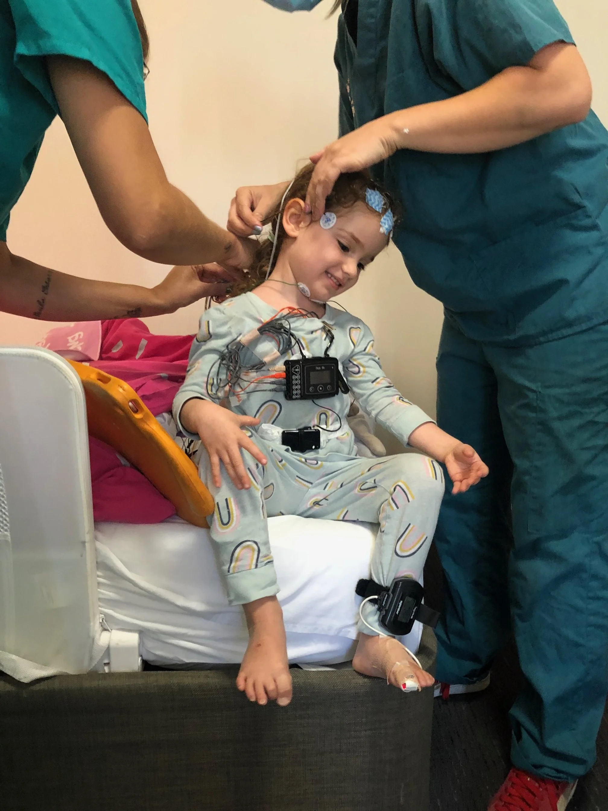 Sasha in a hospital bed surrounded by medical staff connected to monitoring equipment, receiving care for SLC6A1.
