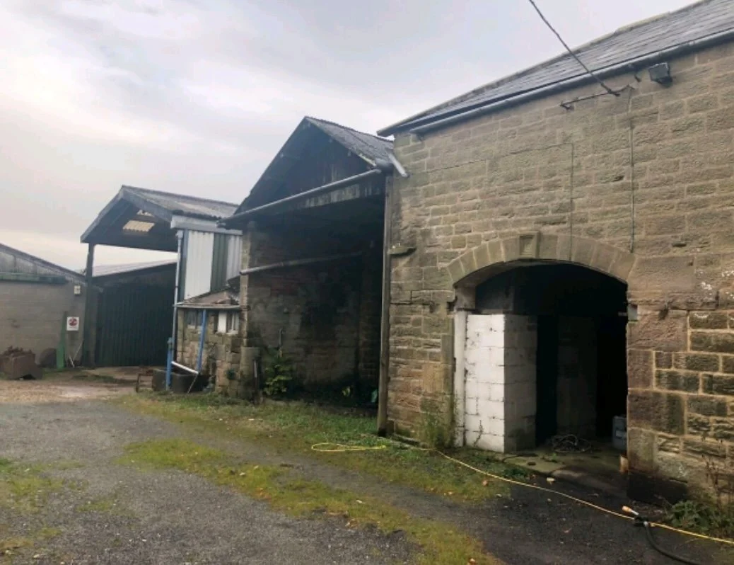 Old stone barn with open archway, weathered brick and metal roofing on overcast day