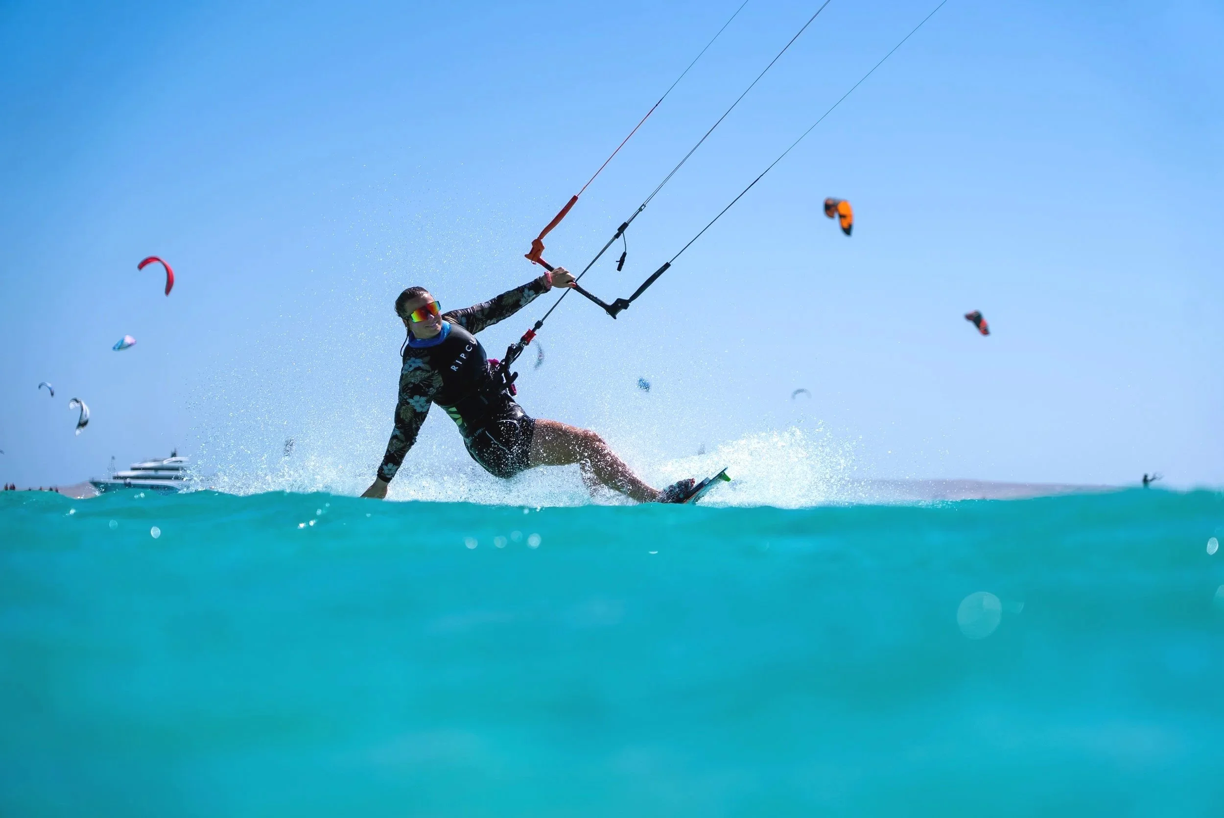 Person kiteboarding on the water with several other kites visible in the sky.