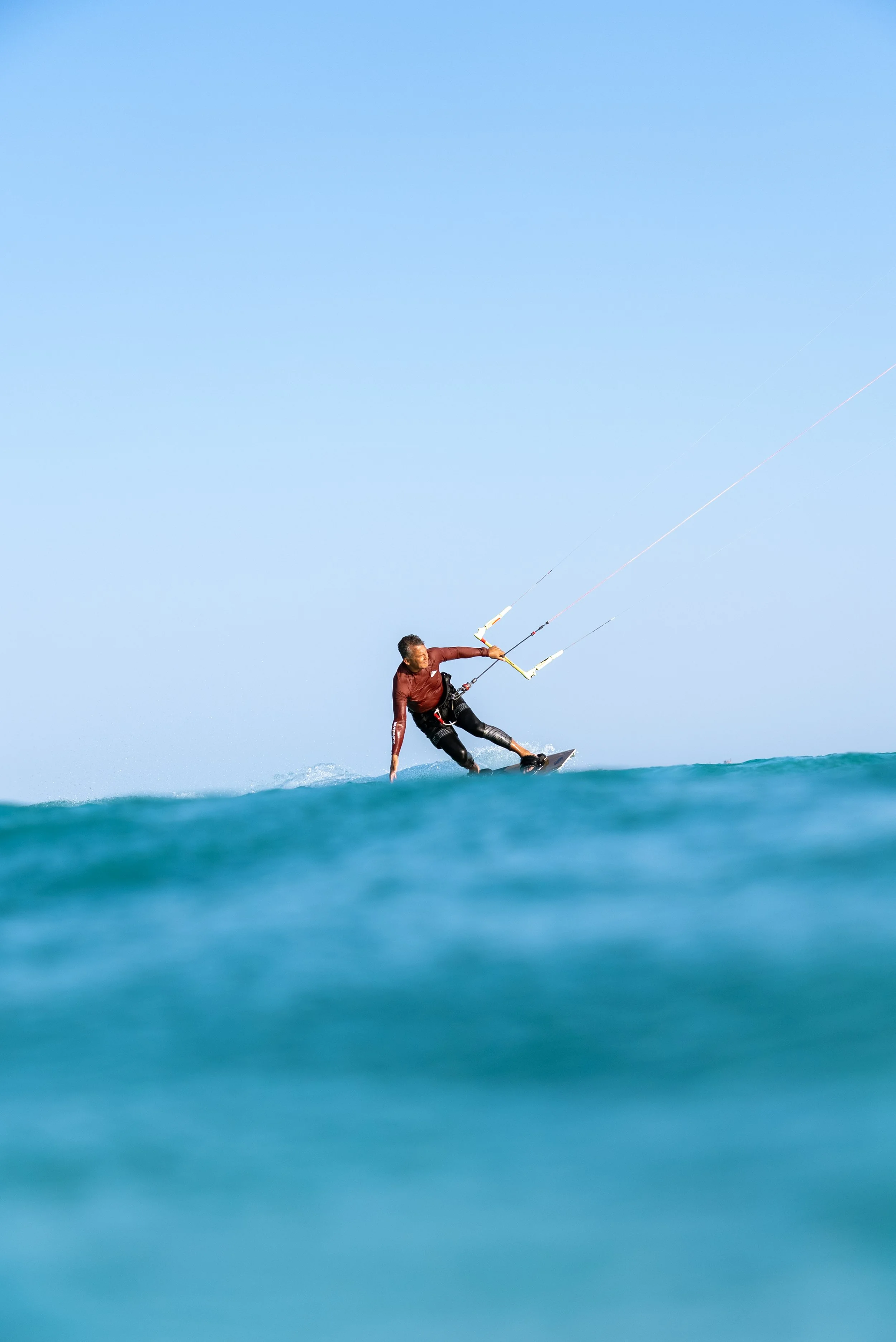 Kite surfer riding a wave in the ocean on a clear, sunny day.