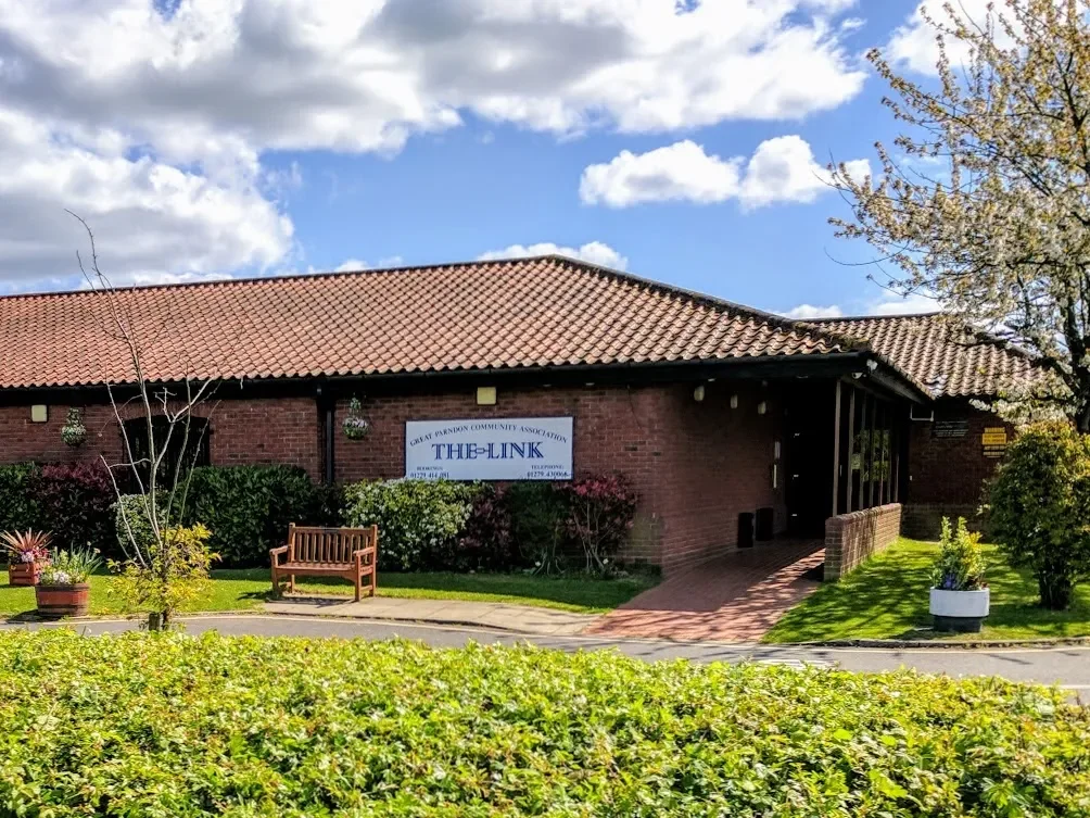 View of a sports stadium with a green field, red and white seats spelling out 'ETSU', and a building with a sloped roof, under cloudy skies.