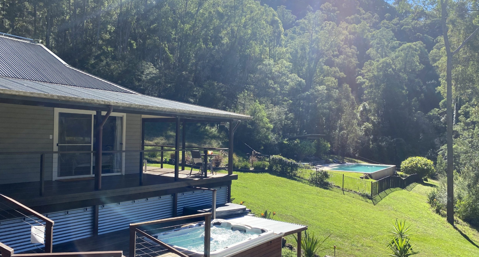 Backyard with deck, hot tub, and swimming pool surrounded by trees and greenery.