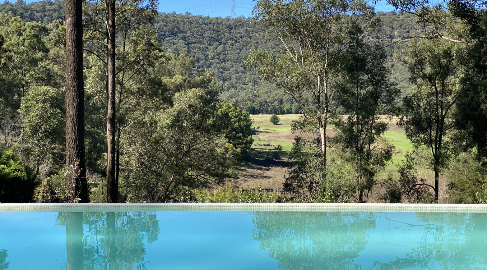 Swimming pool with a nature view of trees and hills in the background, under a clear sky.