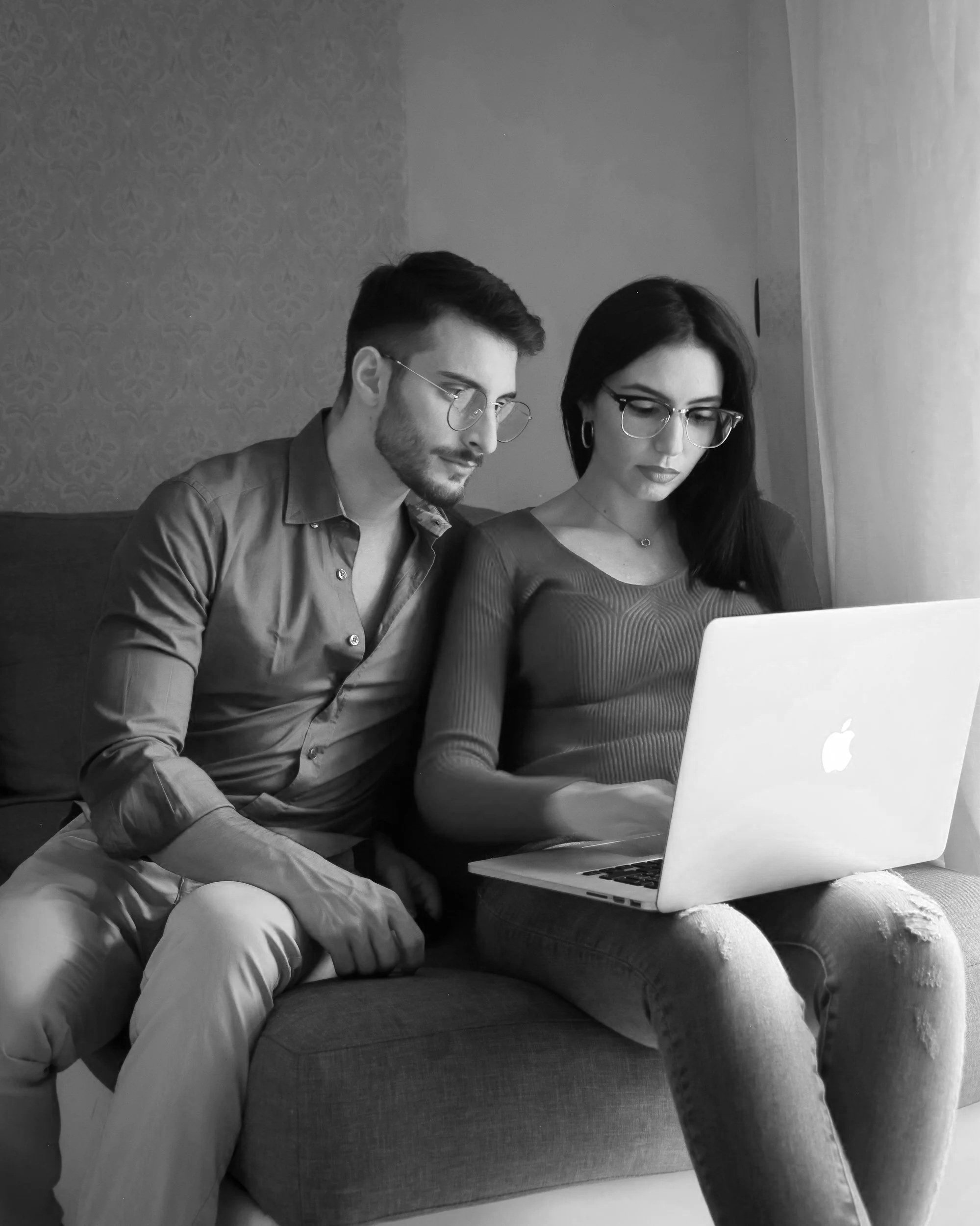terapia de casal online, psicologa debora teodora. Homens e mulher usando óculos, sentados em um sofá, olhando para um laptop branco na frente deles.