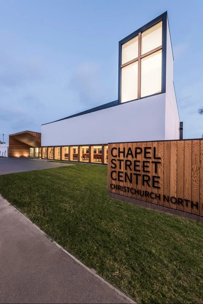 Chapel Street Centre - Modern church building with large glass windows and a wooden sign in front that reads 'Chapel Street Centre Christchurch North'. The church has a white exterior with a prominent tower and is set against a dusky sky.