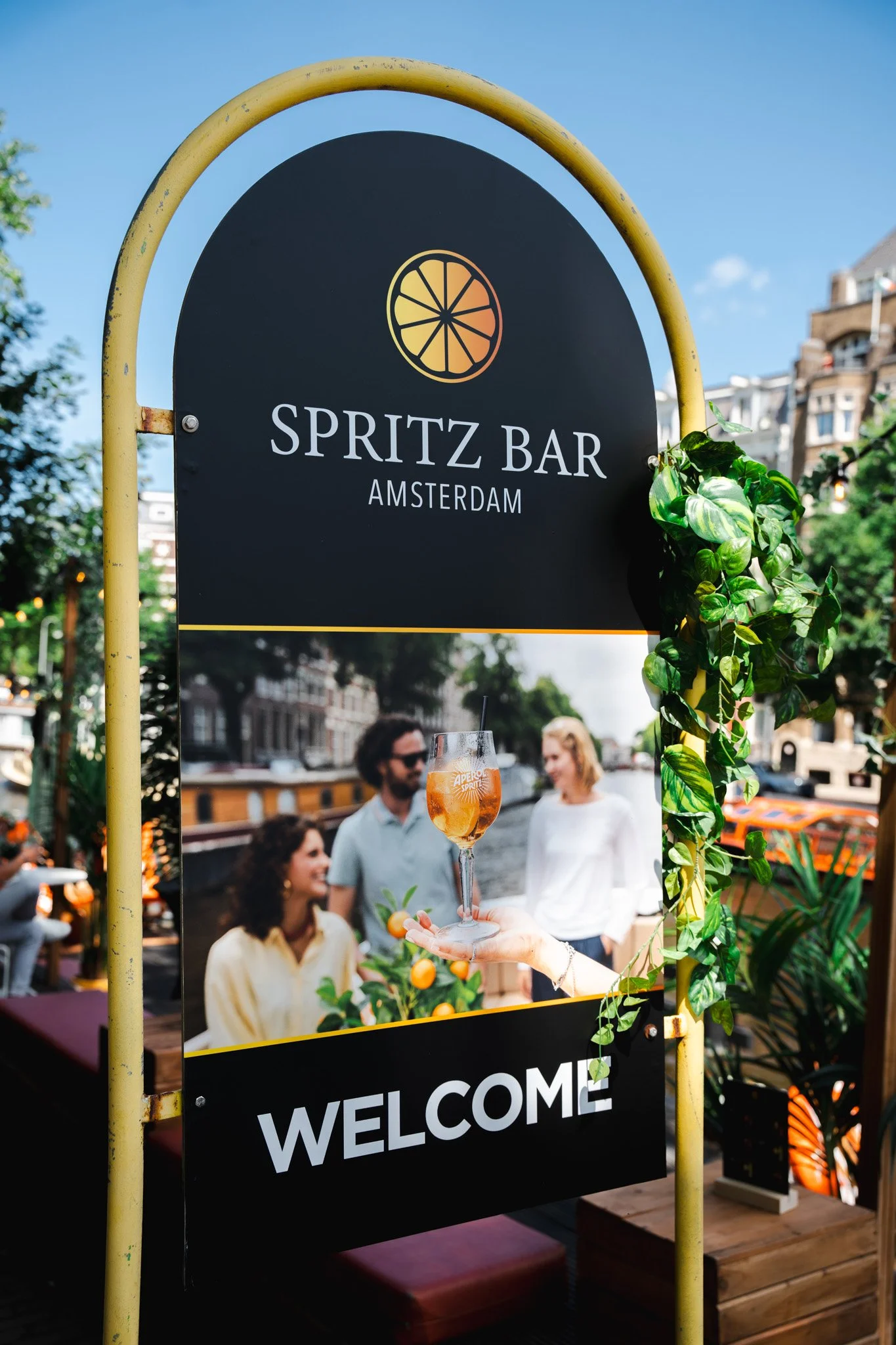 Sign for Spritz Bar in Amsterdam with an image of friends enjoying drinks outdoors by a canal.