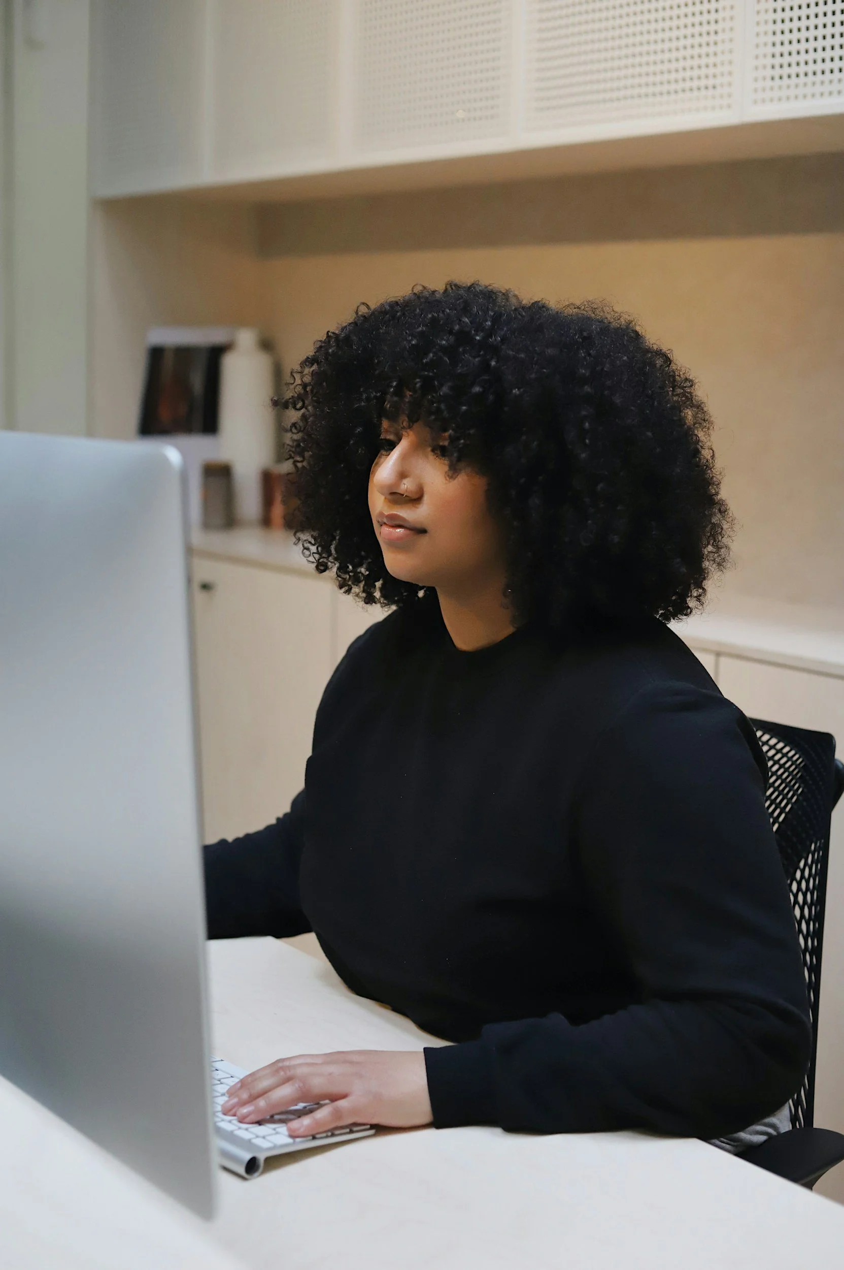 Woman with curly black hair working on a computer in an office setting.