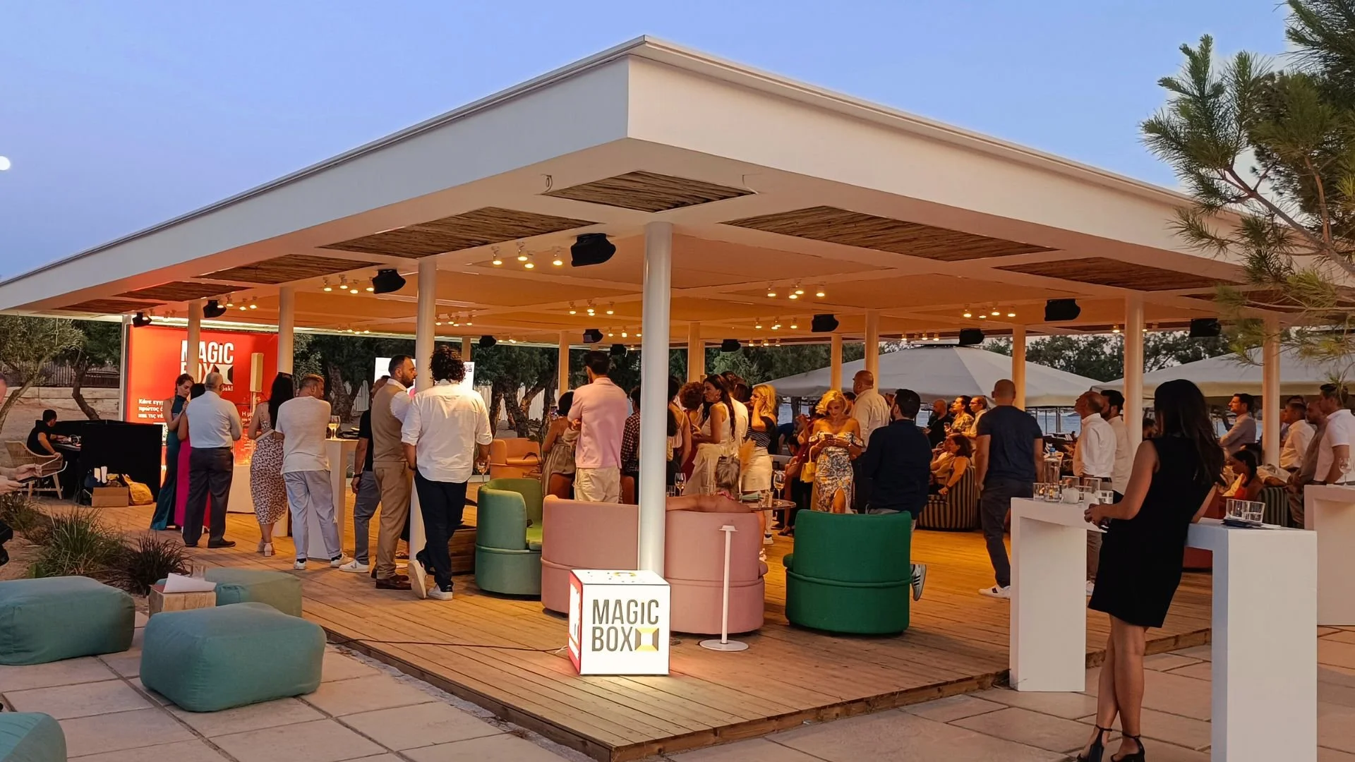 People gathering at an outdoor event under a white canopy with seating and a sign that reads 'MAGIC BOX'.