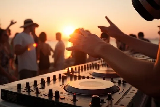 DJ performing at sunset beach party with crowd and ocean in the background.
