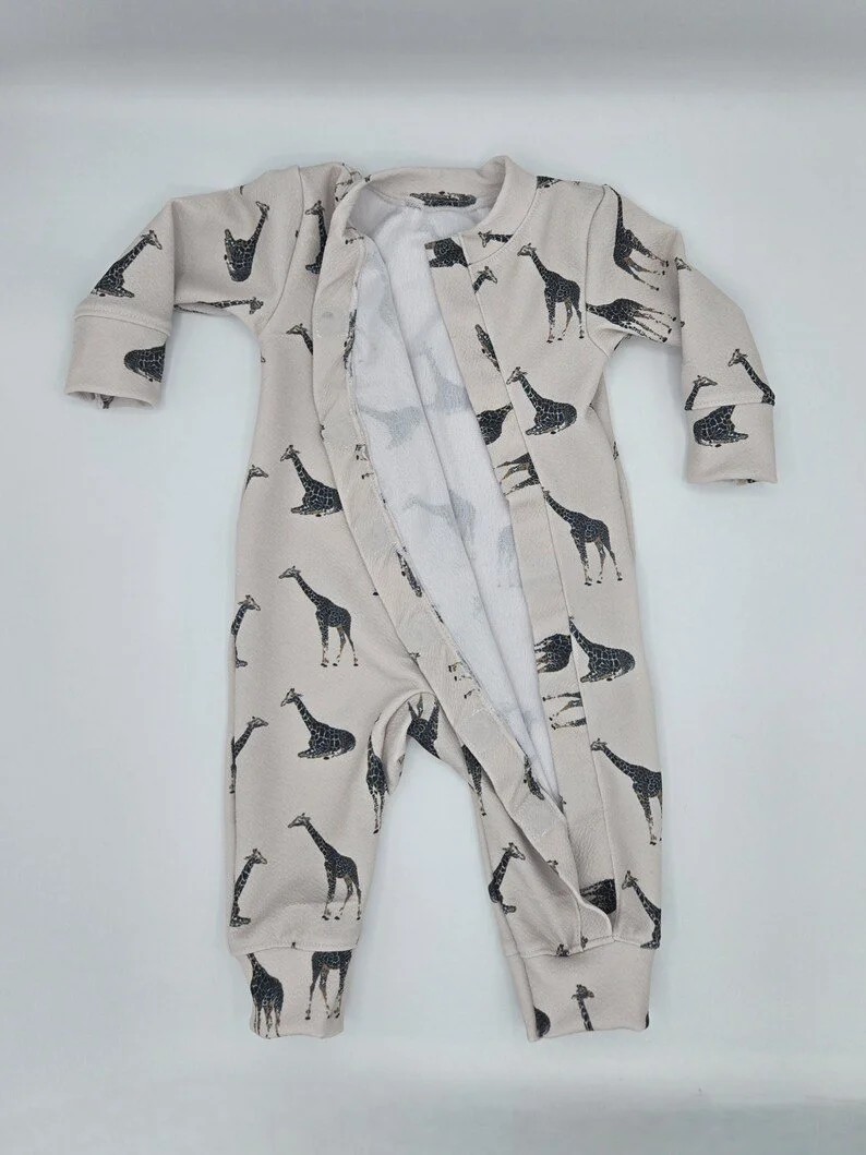 Baby wearing a cream-colored romper with a minimalist giraffe print. The romper opens in the front.