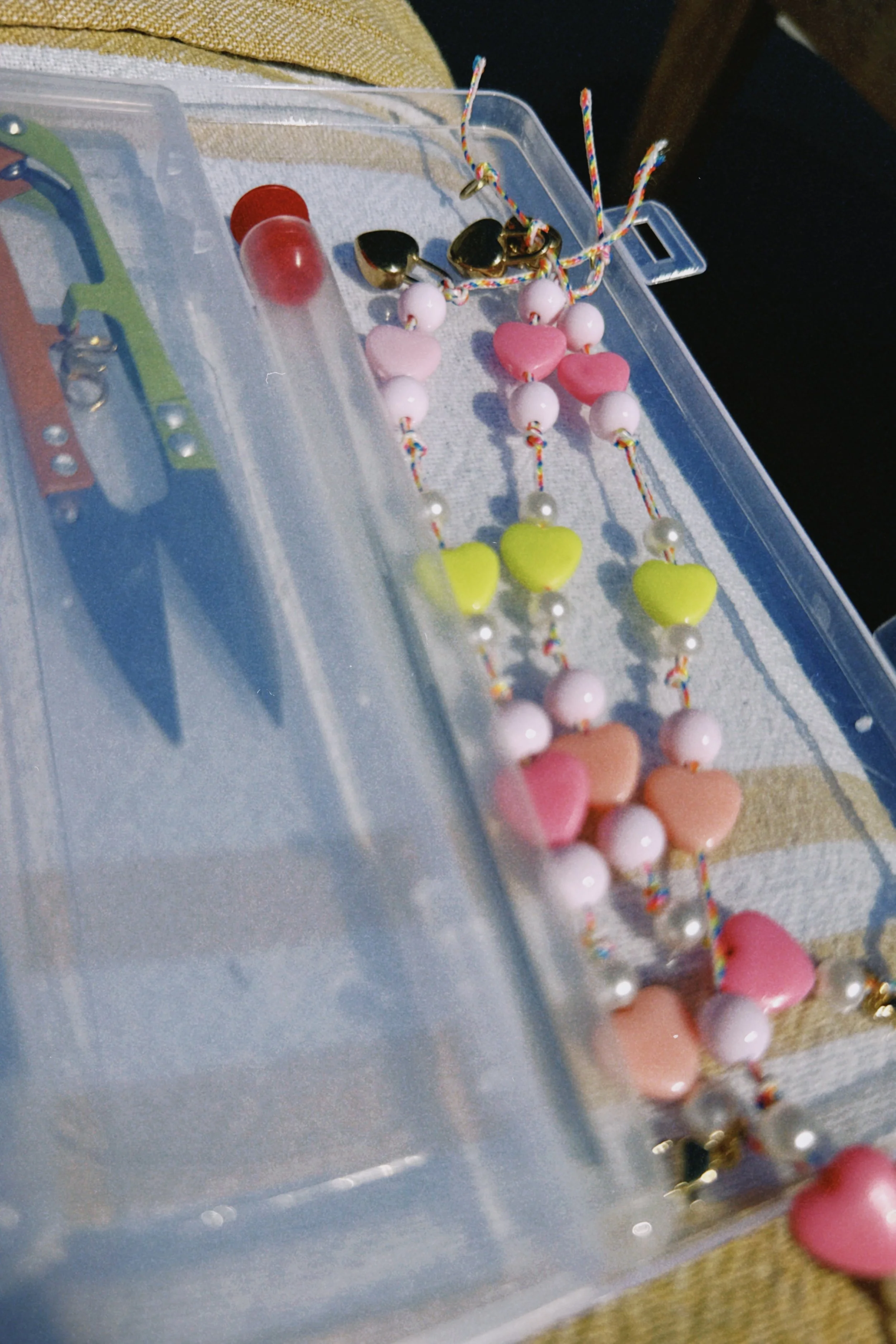 Colorful heart-shaped and round beads inside a plastic jewelry box with an attached string of beads.