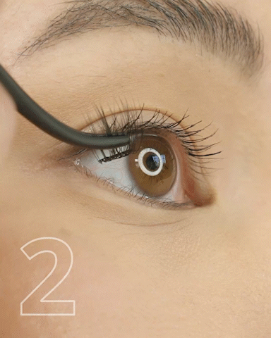 Close-up of a person applying makeup or adjusting their eye with a black tool, focusing on the brown eye and eyelashes.