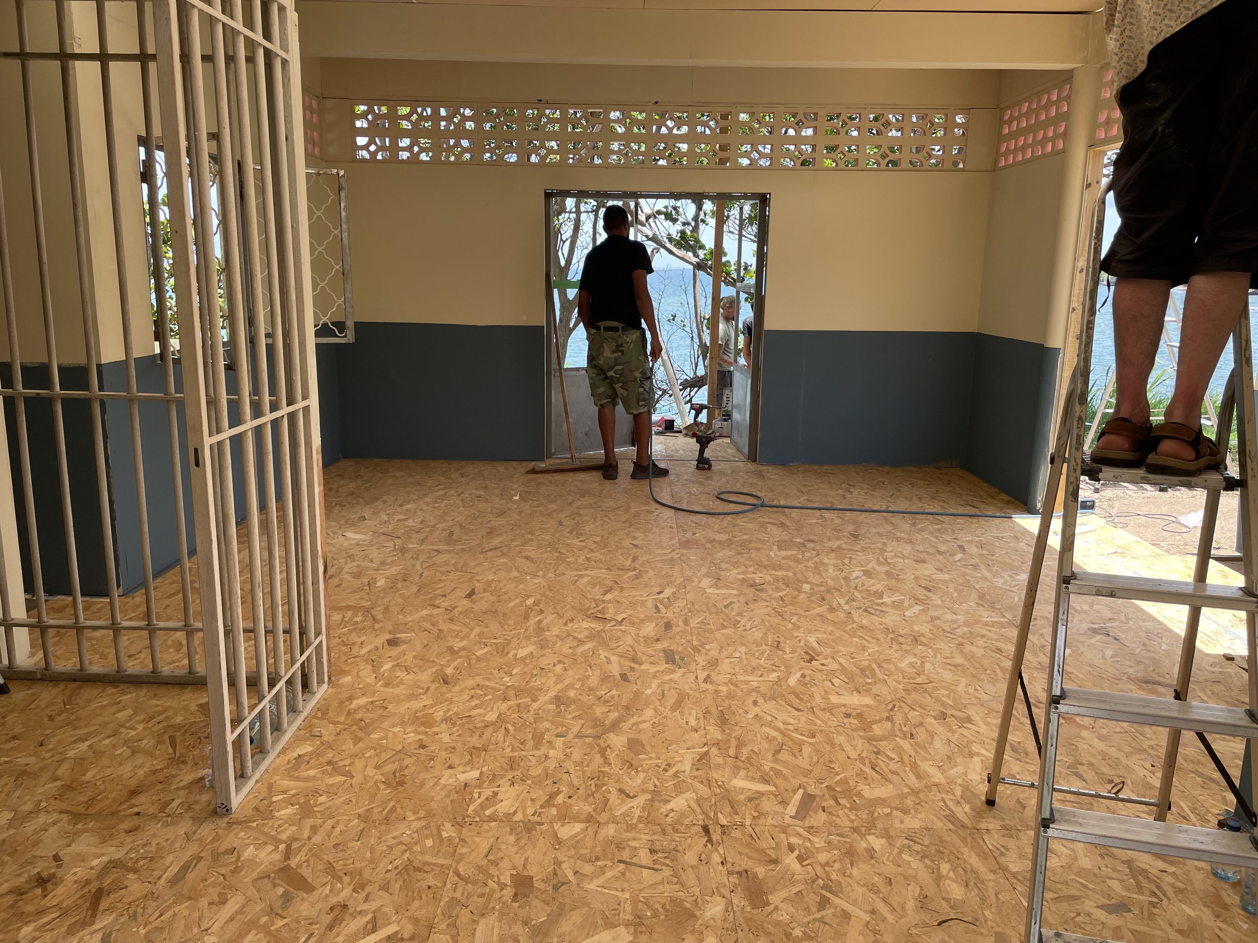 Room under construction with workers installing a door to an outdoor patio with trees and a view of the water.
