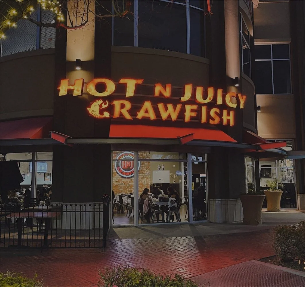 Exterior view of Hot N Juicy Crawfish restaurant at night with illuminated signage and guests inside.